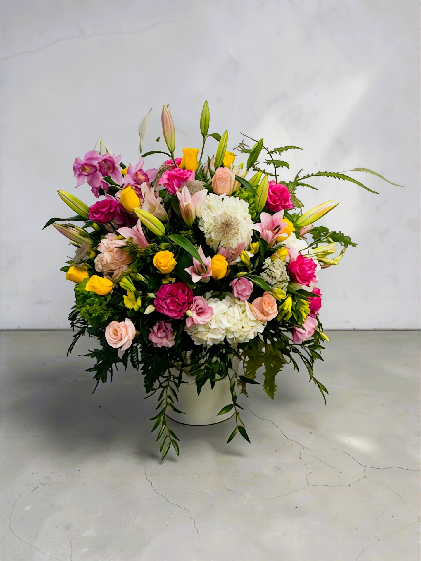 Love &amp; Romance by Daisy - A bright, cheerful mixed flower arrangement that makes anyone feel celebrated-perfect as a birthday bouquet, thank-you gift, or just-because surprise. Live, Love, Smile by Daisy pairs pink, yellow, white and soft peach blooms in a full, rounded design so the recipient feels seen the moment it arrives.  This large, abundant arrangement is built in a clean white container and layered with lilies, roses, carnations, chrysanthemums and alstroemeria. Long lily buds and airy greenery add height and movement while dense clusters of rose-like blooms and chrysanthemum accents create a lush, textured look; the palette reads fresh and springlike from every angle.  Send this arrangement to mark congratulations, brighten someone's day, or celebrate a special moment-she'll feel genuinely cheered by the color and scent. Delivered ready to display in its container; for longest enjoyment, keep in a cool spot away from direct sun and refresh the water every couple of days.
