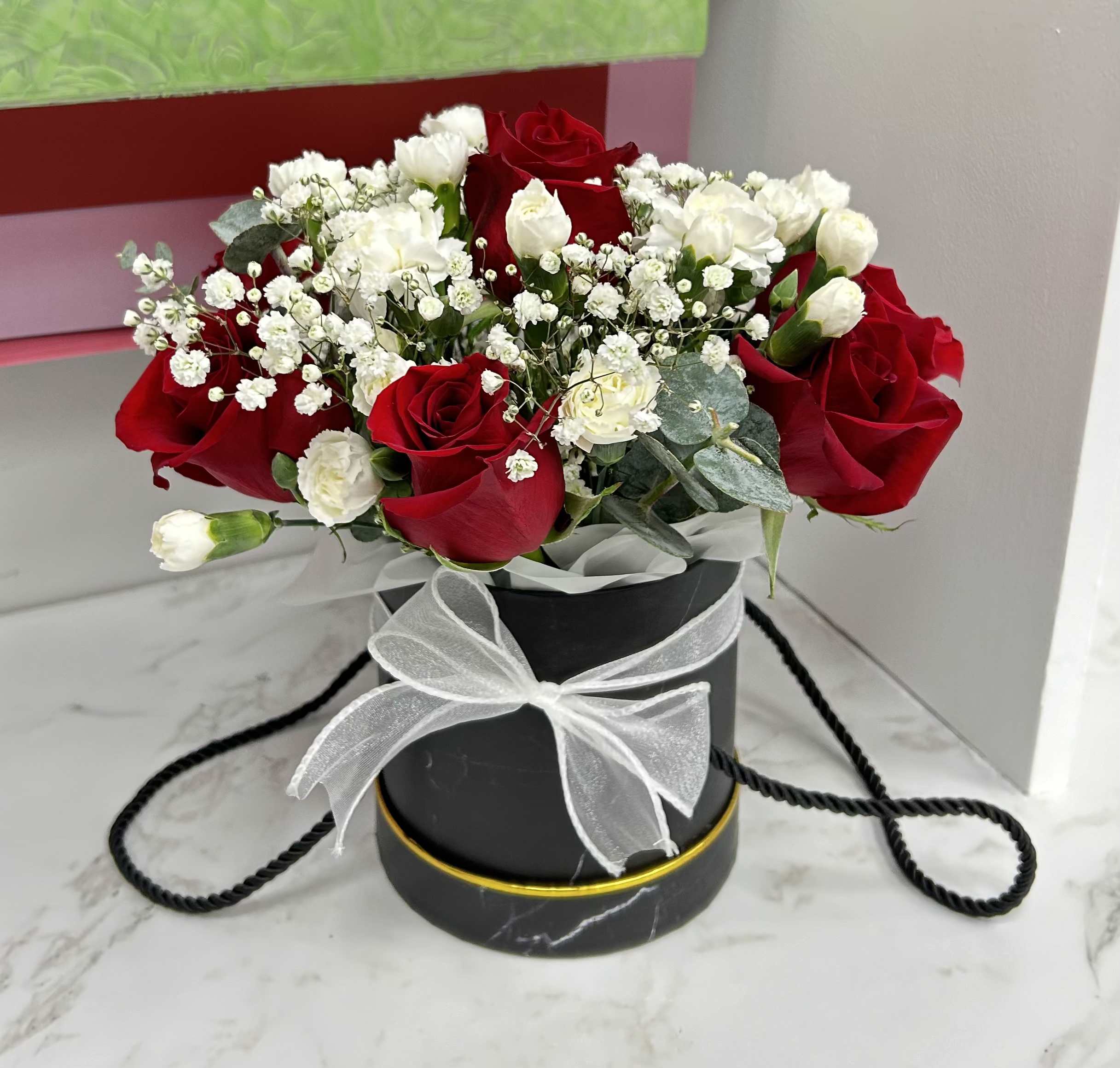 Red and white rose arrangement in a black round box with a white ribbon