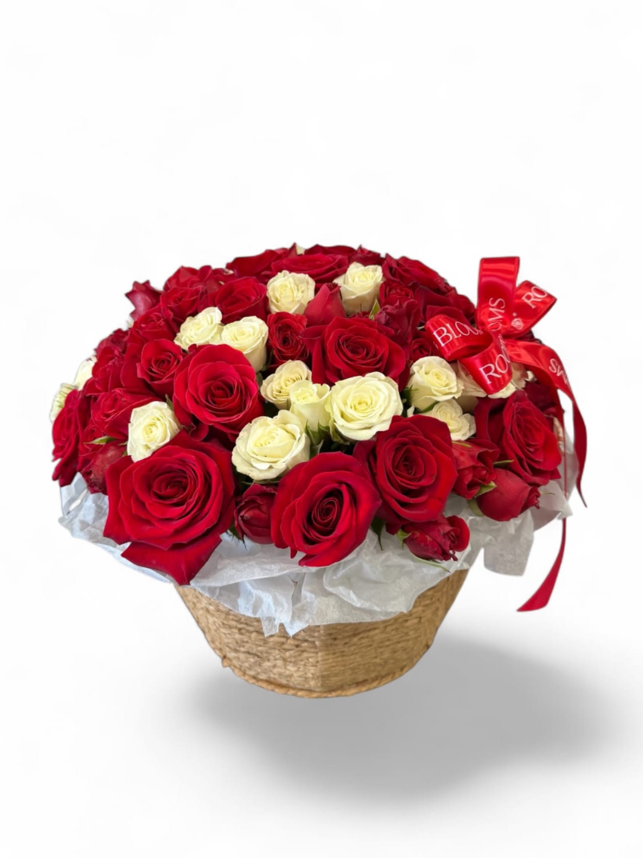Red and white roses arranged in a woven basket with a red ribbon