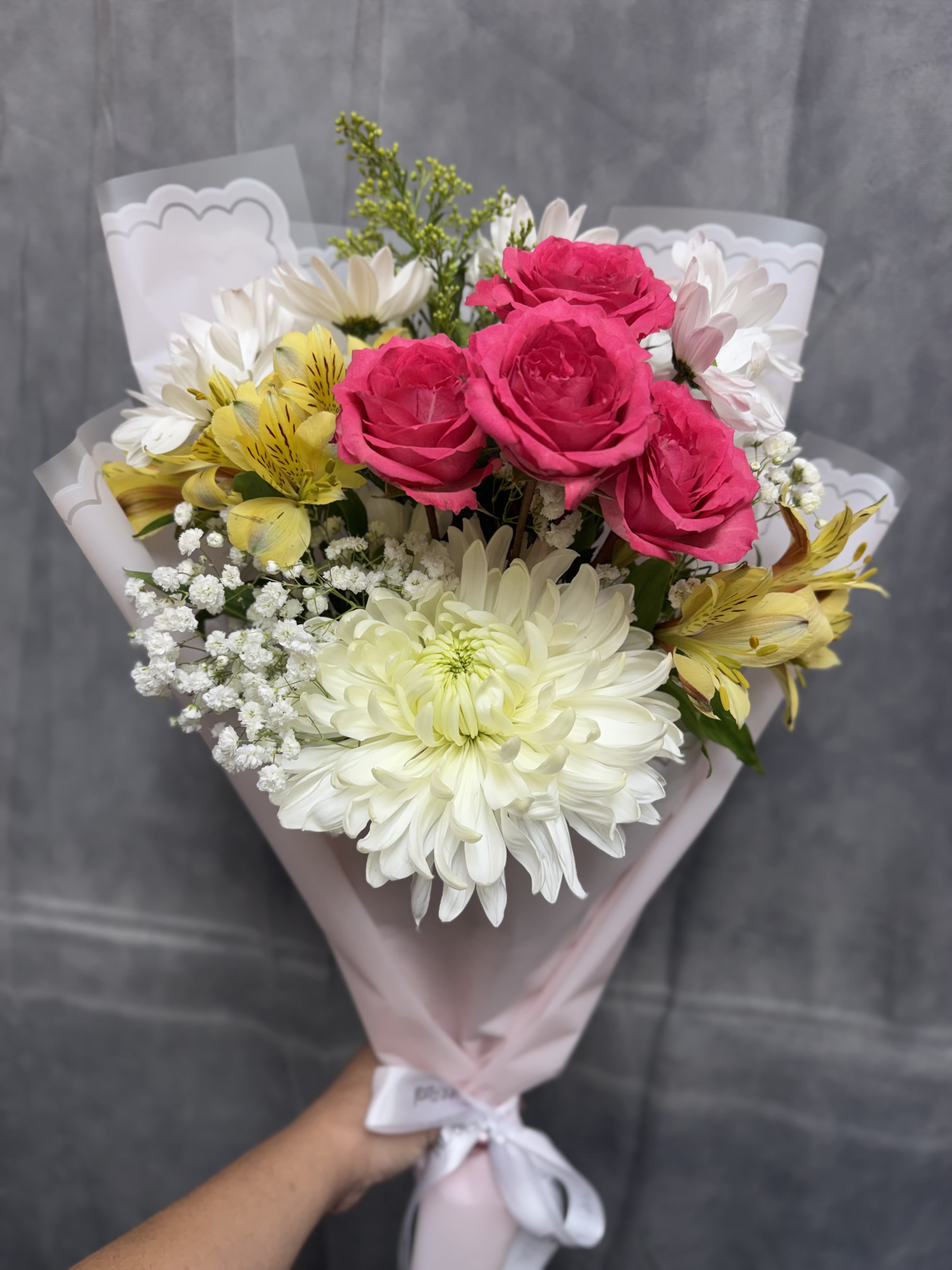 Pink Breeze Bouquet  - Our petite Pink Breeze hand-tied bouquet features cheerful mums, spray roses, daisies, and alstroemeria , all wrapped in soft pink paper for a sweet, charming touch — perfect for brightening someone’s day.