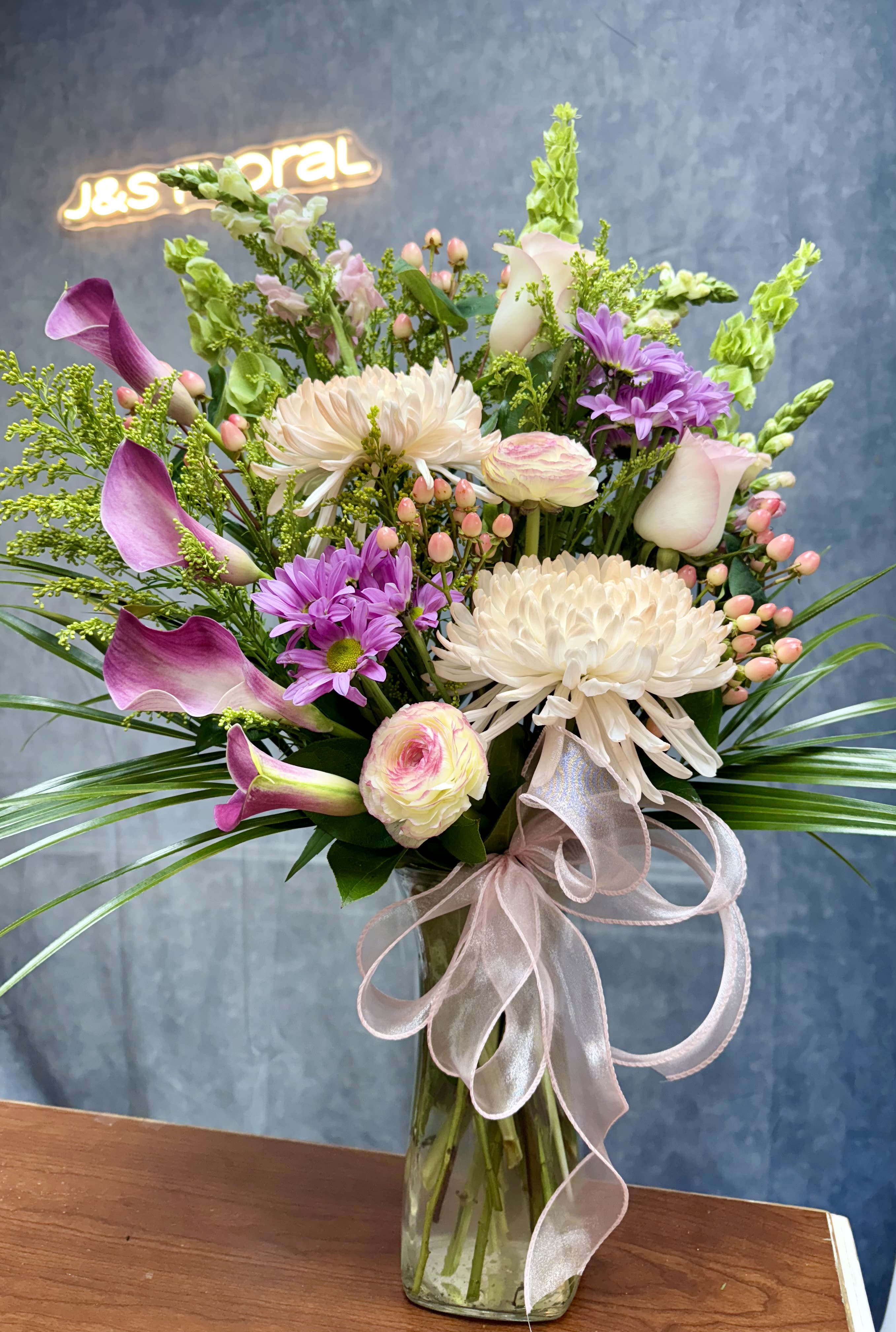 Charming Blooms  - A stunning blend of elegant Calla lilies, lush mums, and delicate ranunculus, this arrangement exudes timeless beauty and sophistication. Perfect for expressing love, sympathy, or simply adding a touch of refined charm to any space.