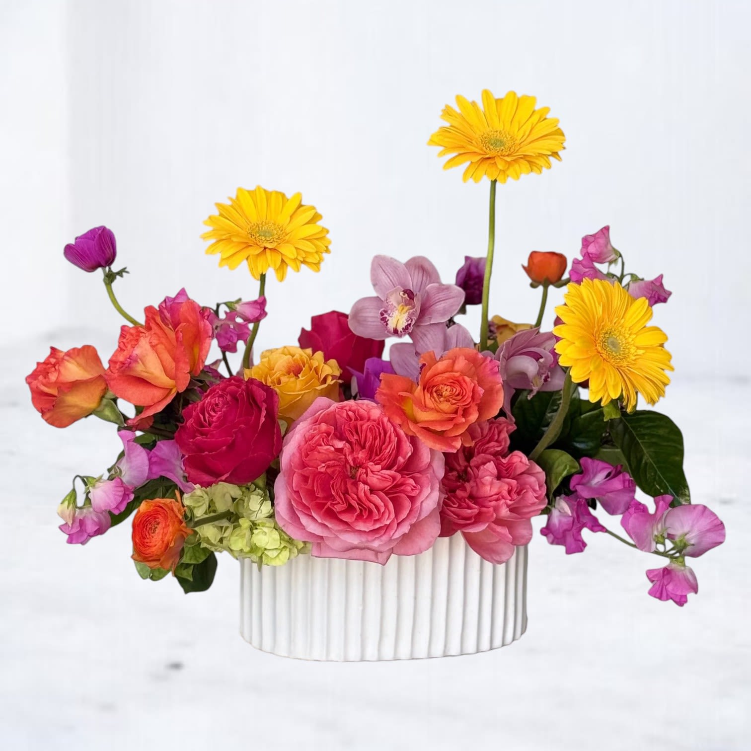 Fruit Punch - Fruit Punch is a vibrant explosion of color featuring lush pink garden roses, sunset orange roses, golden gerbera daisies, orchids, sweet peas, and playful seasonal blooms arranged in a modern white ceramic vessel. Bursting with juicy pink, coral, orange, and yellow tones, this design feels energetic, artistic, and full of personality.  Perfect for birthdays, celebrations, thank-you gifts, get-well wishes, or simply brightening someone’s day, Fruit Punch brings bold color and modern floral design together in one unforgettable arrangement. Designed with premium seasonal flowers and natural movement for an elevated editorial look.  Available for same-day flower delivery in Magnolia, The Woodlands, Montgomery, Conroe, Spring, Tomball, and surrounding Houston areas.