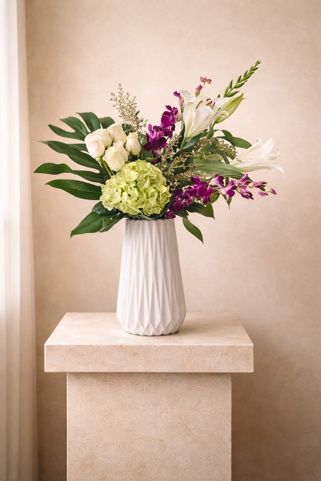 Tall white vase with white roses, lilies, green hydrangea and purple orchids with large tropical leaves.