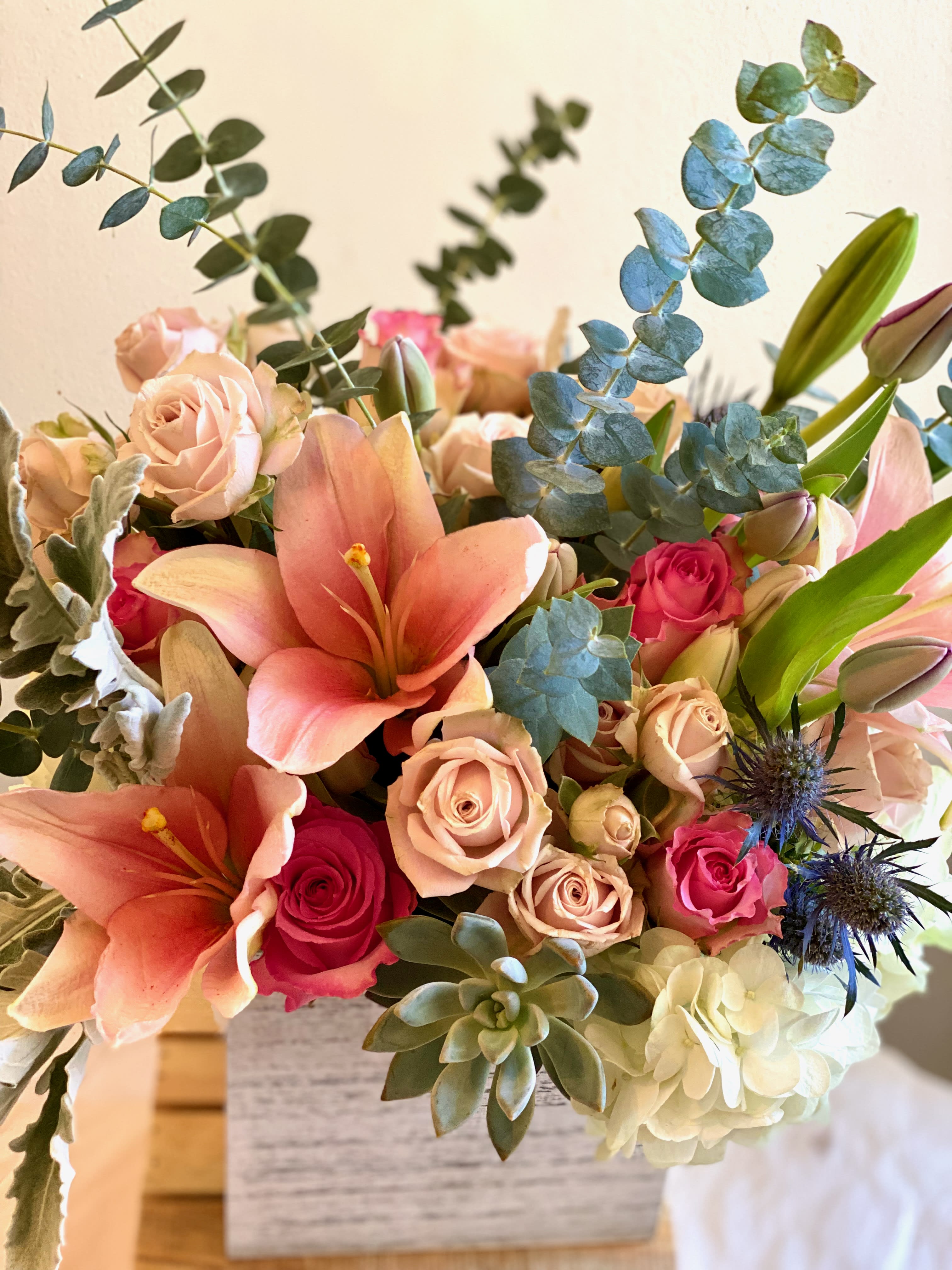 Bouquet of peach lilies, pink roses, and eucalyptus in a vase