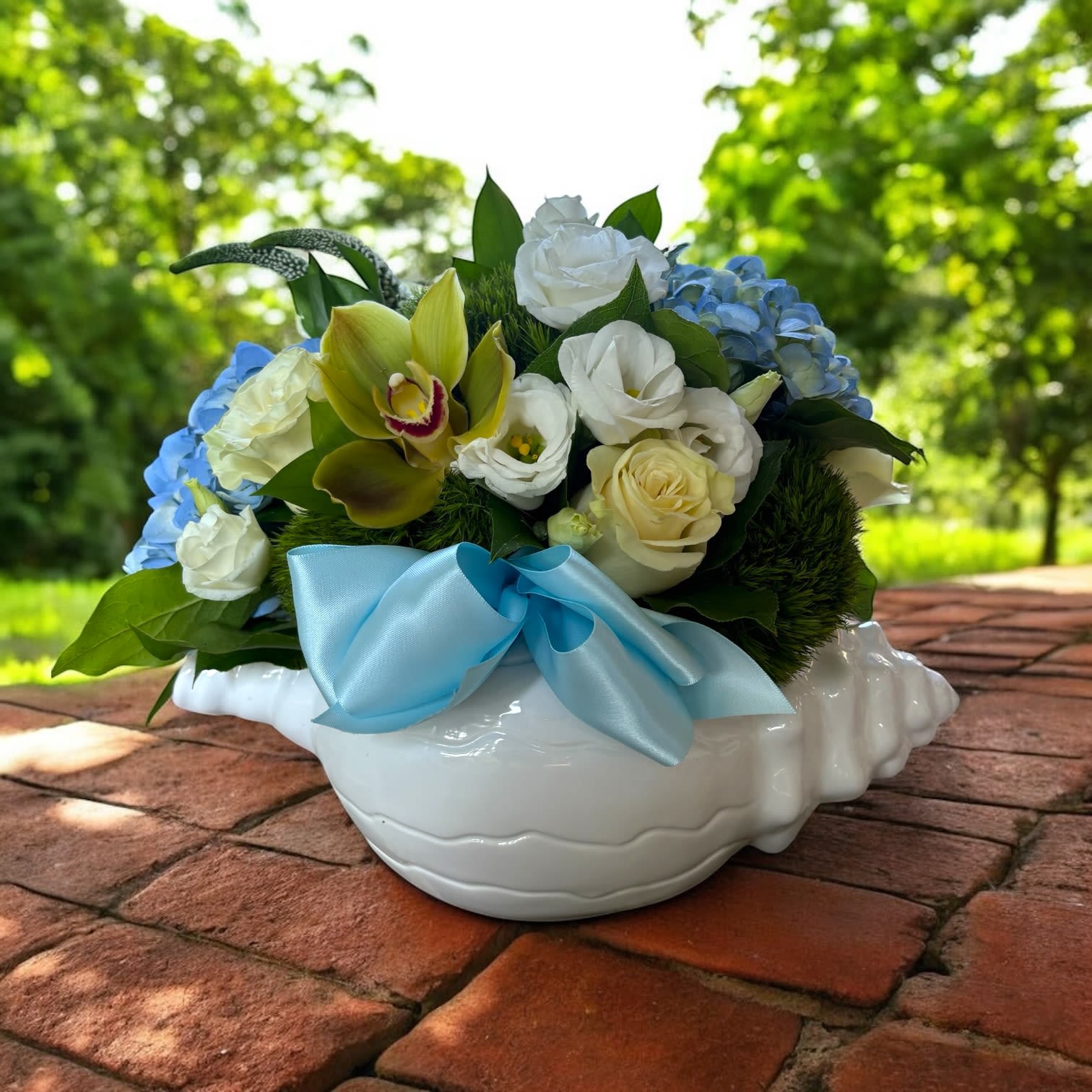 Bouquet of white and blue flowers in a white ceramic bowl with a blue ribbon