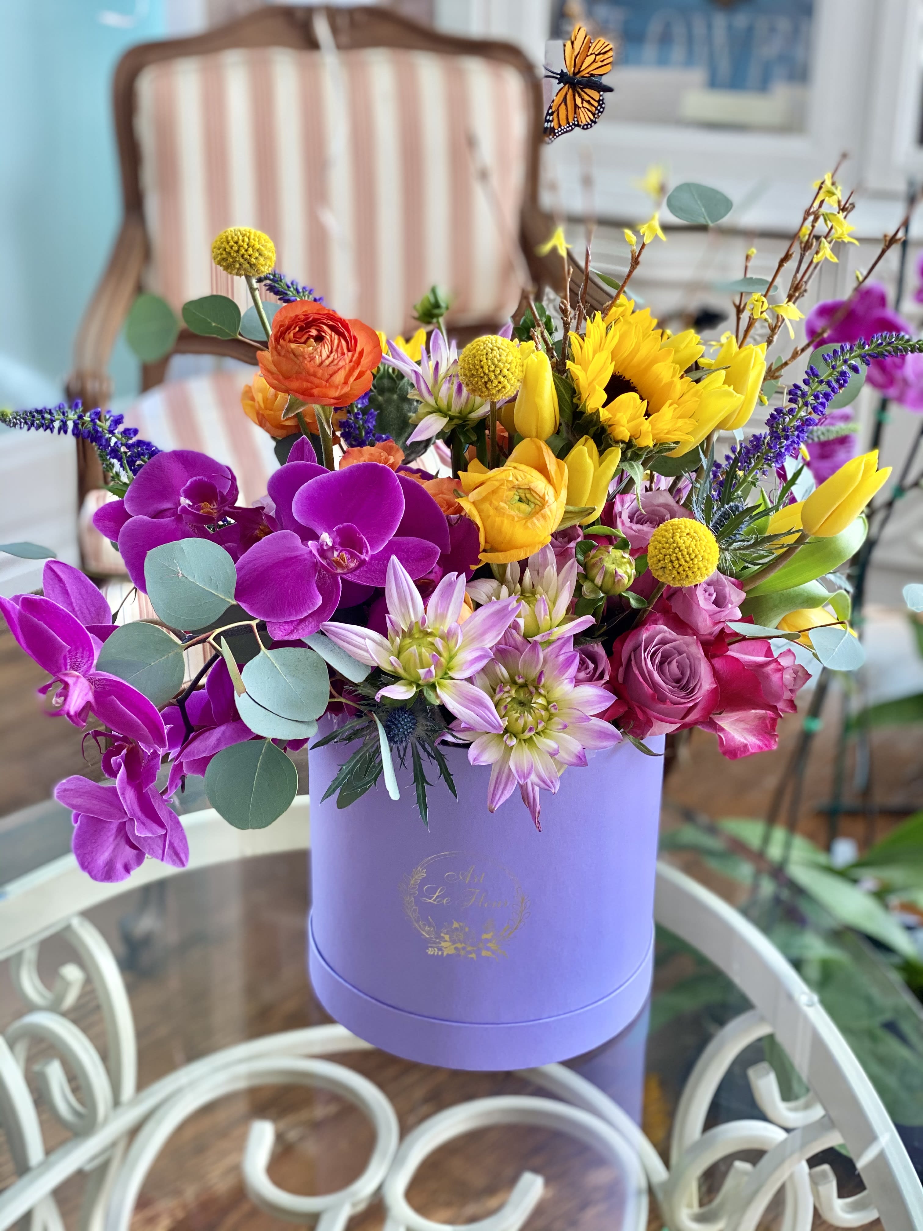 Colorful mixed bouquet in a lavender hat box with orchids, roses, and sunflowers