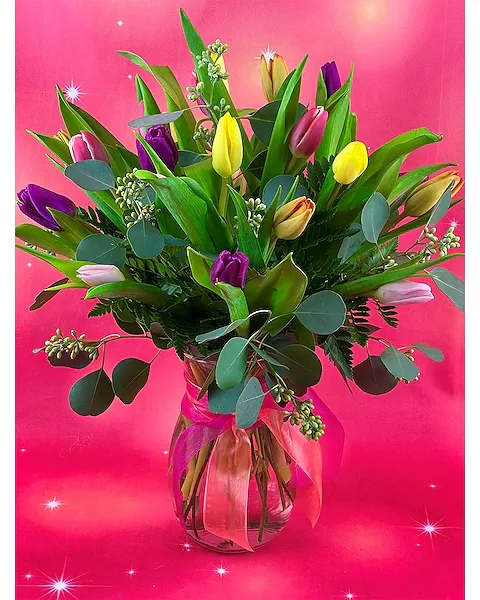 Vase of mixed-color tulips with lush foliage and ribbon on a bright pink background