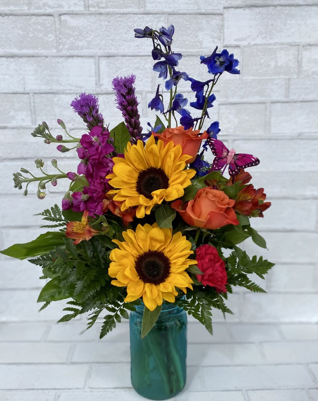 Colorful mixed bouquet in a teal glass vase with sunflowers and roses