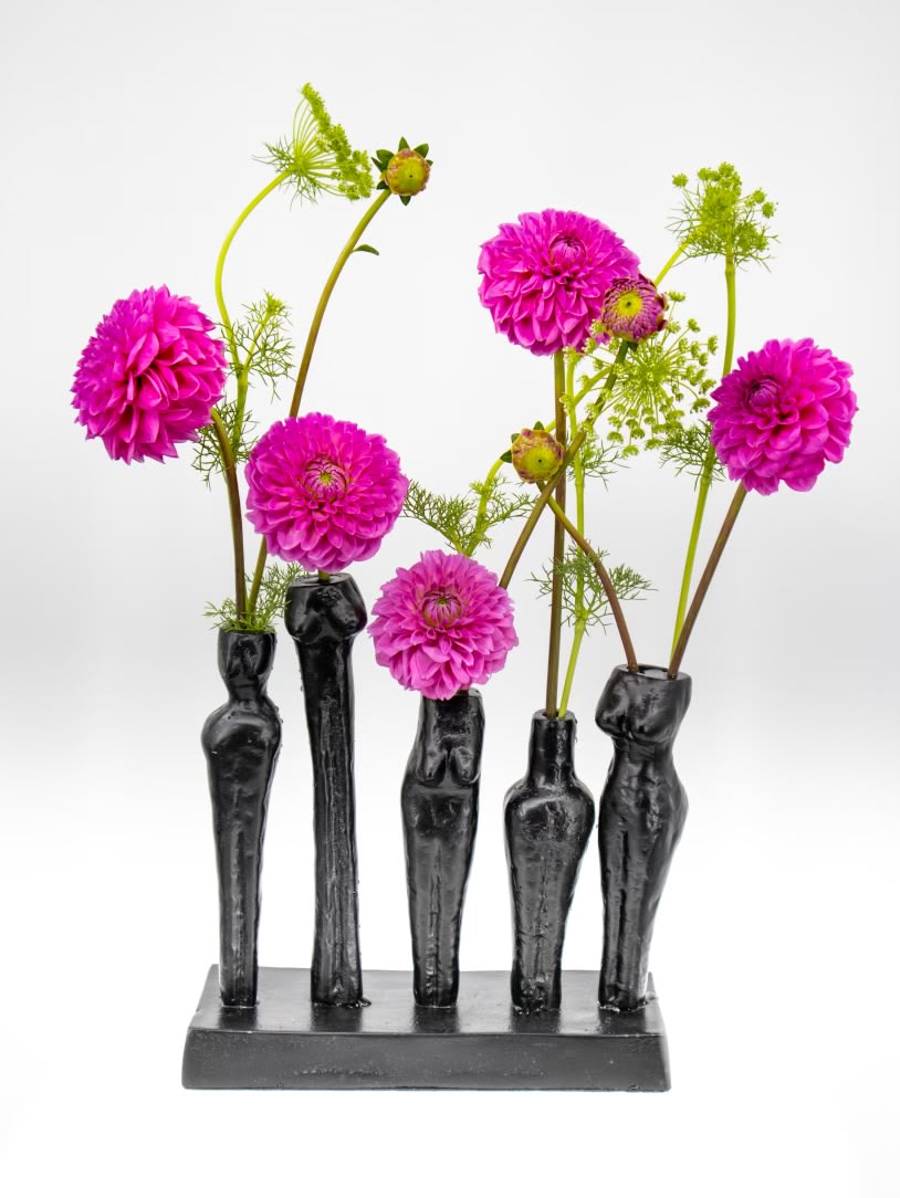 Five magenta flowers arranged in black sculptural vases on a rectangular base.