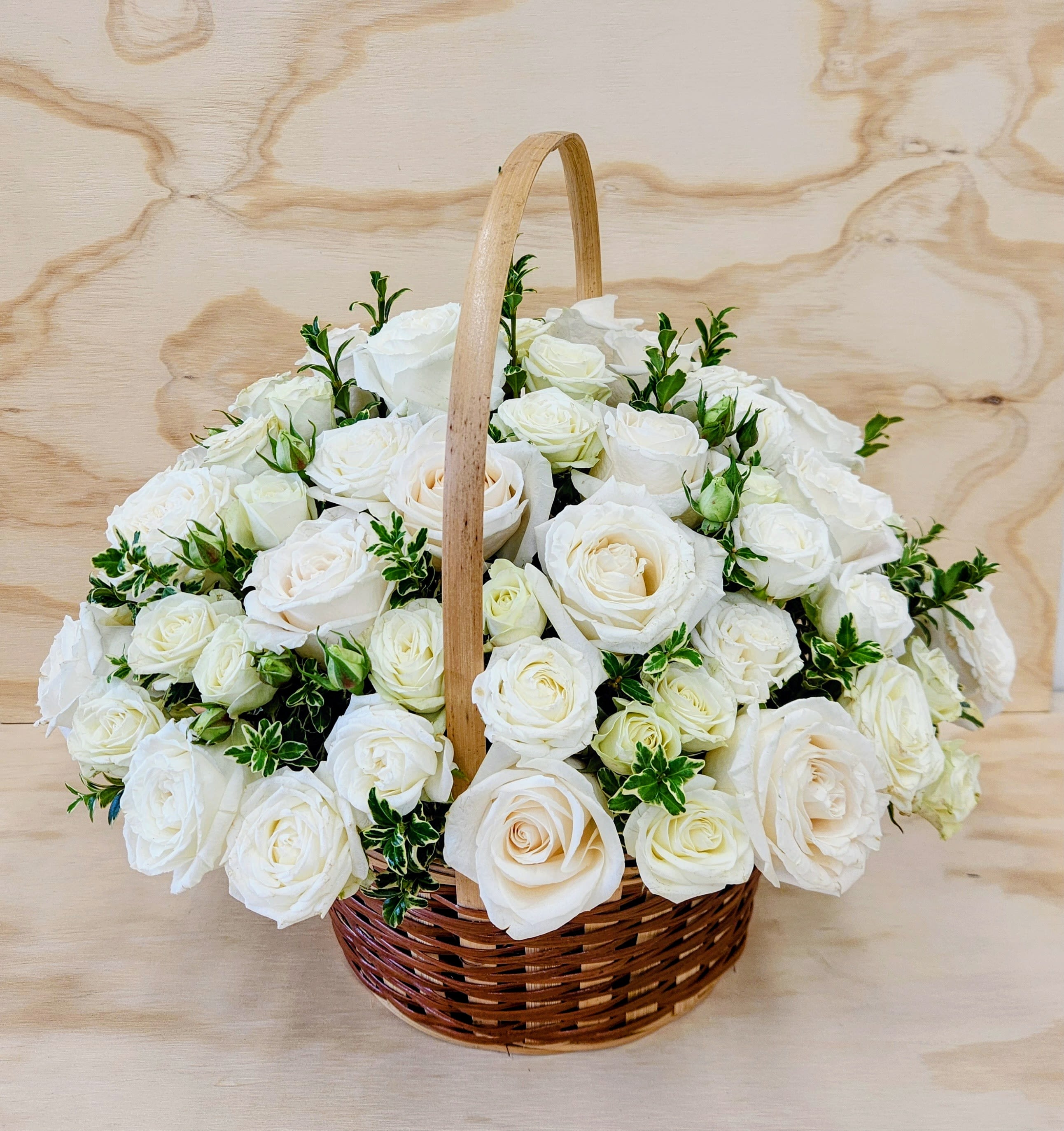 Classic White - A round cluster of white roses gathered in a hand-carried wicker basket creates an elegant, understated gift perfect for wedding celebrations or a sympathy arrangement. The soft, all-white palette reads as timeless and serene, so the person you're thinking of will feel comforted and honored whether you're marking a milestone or offering sympathy. PREMIUM SIZE ONLY. 15" by 15"  
