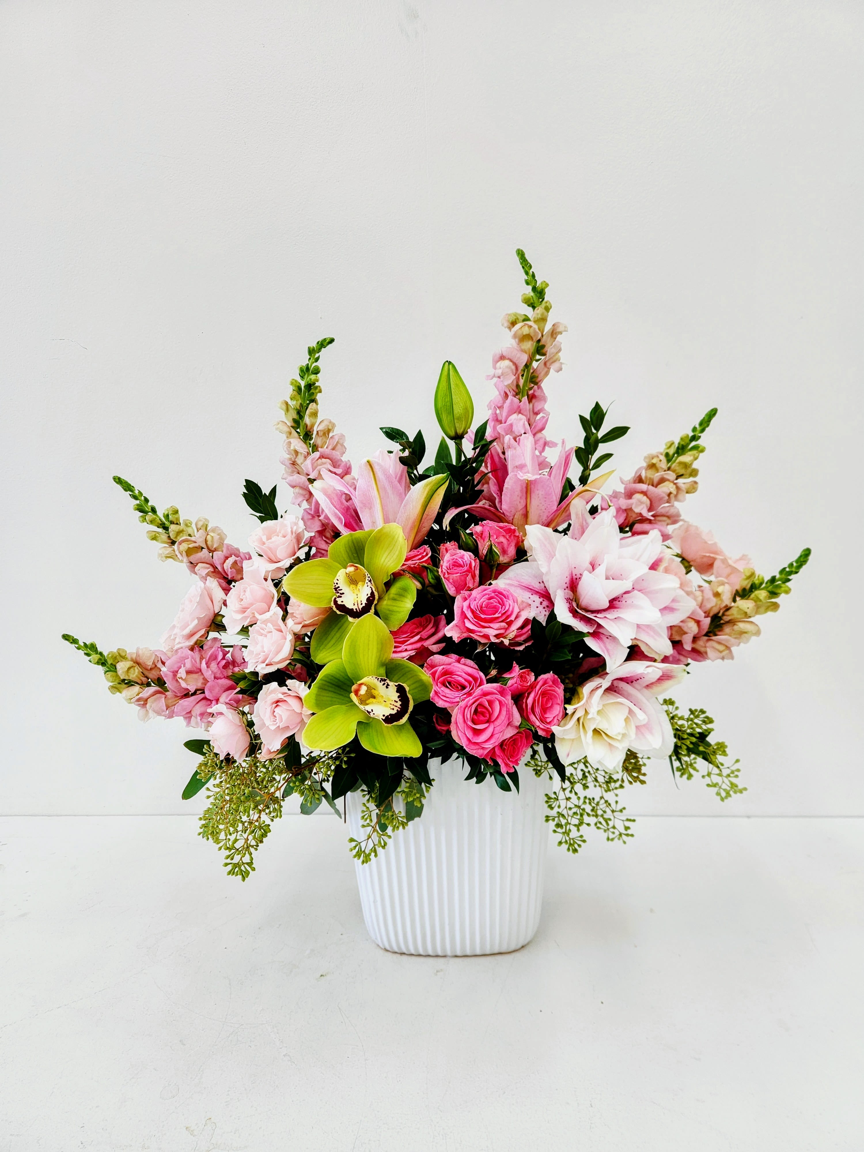 Pink Glow - A lush cascade of full and symmetrical design of pink roses and pale lilies gives this flower arrangement a tender, celebratory feel-perfect as a birthday bouquet, a Mother's Day surprise, or a "just because" gift to make someone feel truly seen. Pink Glow pairs romantic pinks and creamy whites with vivid chartreuse orchids for a fresh, modern twist that reads both springtime and special-occasion ready. 