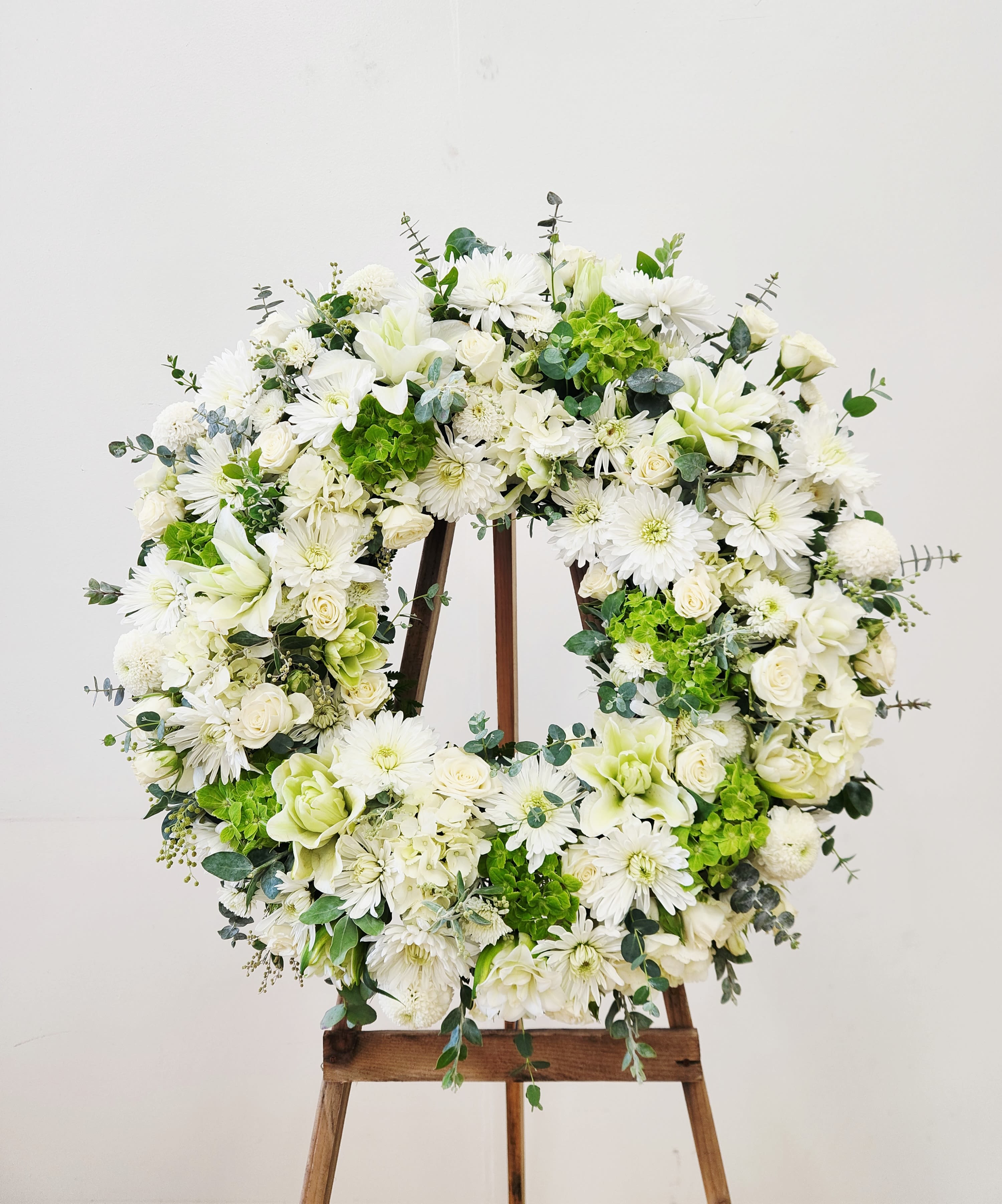 Everlasting  - A serene circular sympathy wreath in white and green creates an immediate sense of calm and remembrance - the kind of memorial or service tribute that lets the person you're honoring feel truly seen. This large easel-mounted arrangement reads formal yet fresh, making it equally appropriate for a funeral service, memorial, or a refined celebration like a wedding or commemorative event where a tranquil presence is needed. CALL US FOR ANY SPECIAL REQUEST. 562-437-4106 or Visit us at 611 E Carson Street, Suite B, Long Beach, CA 90807  