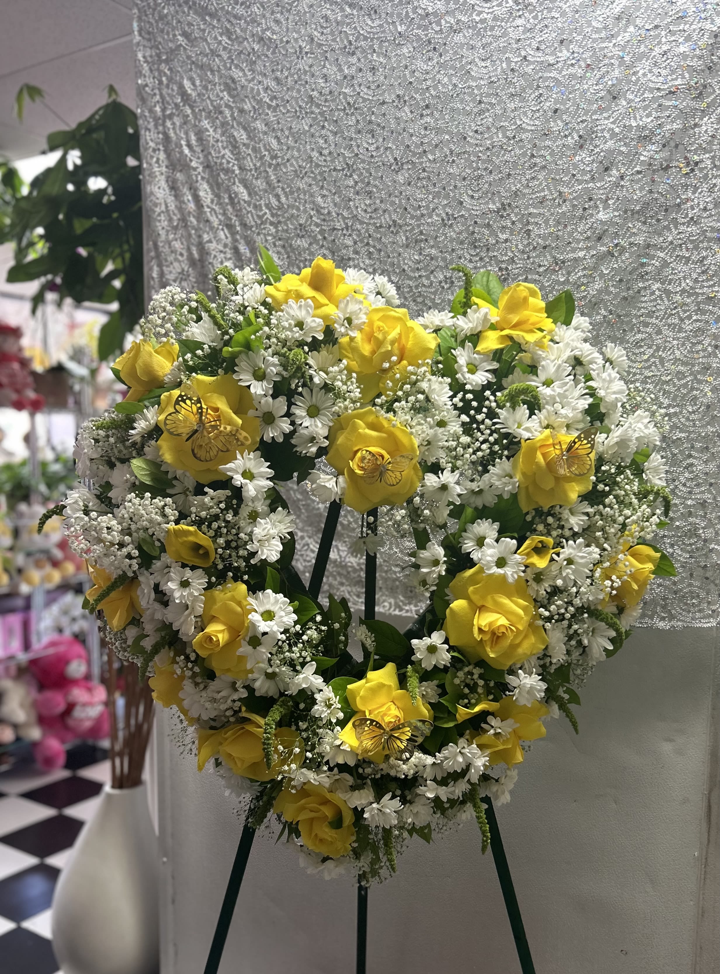 Heart-shaped floral wreath with yellow roses and white daisies on an easel