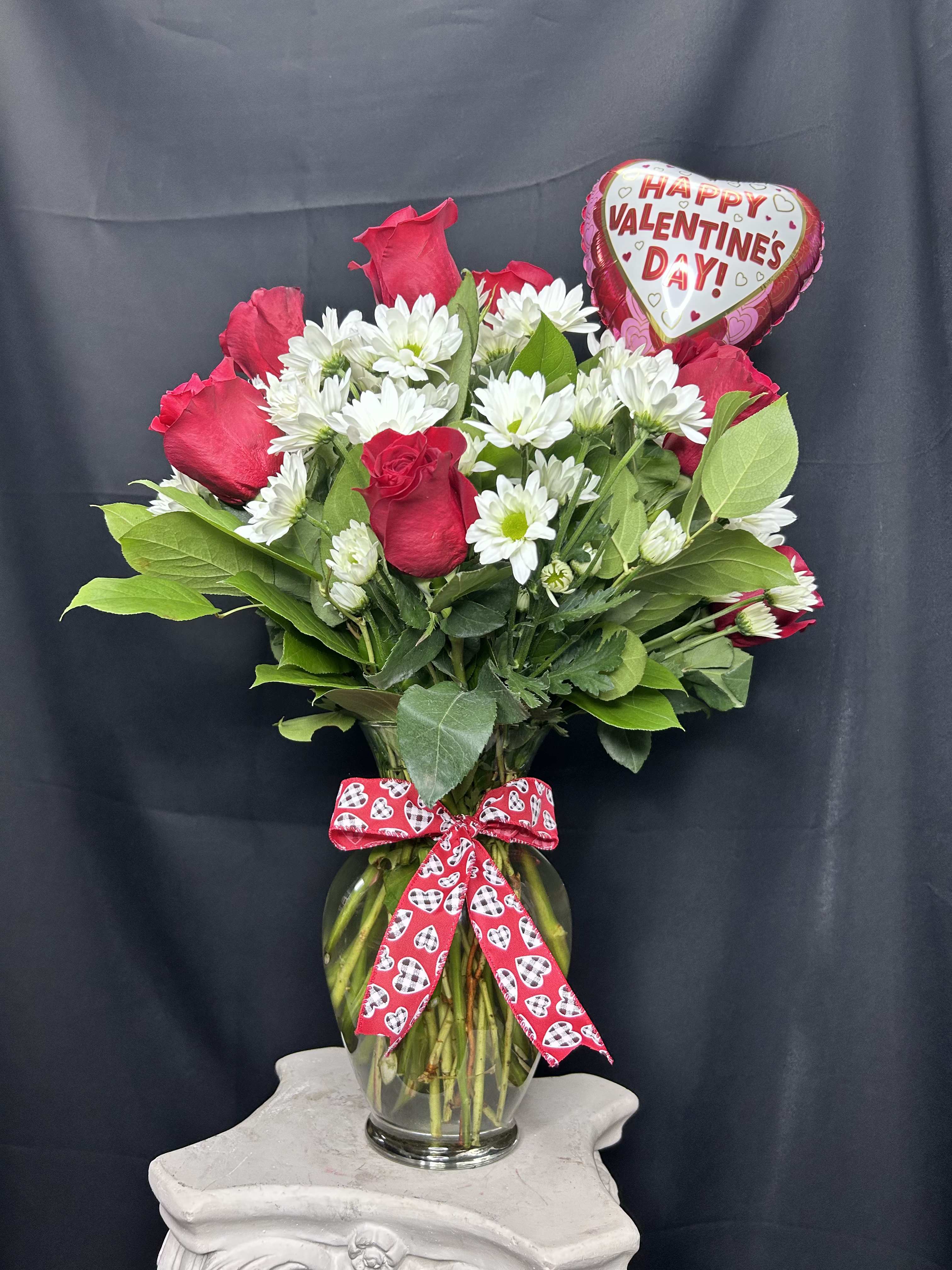 Red roses and white daisies in a glass vase with a Valentine heart balloon