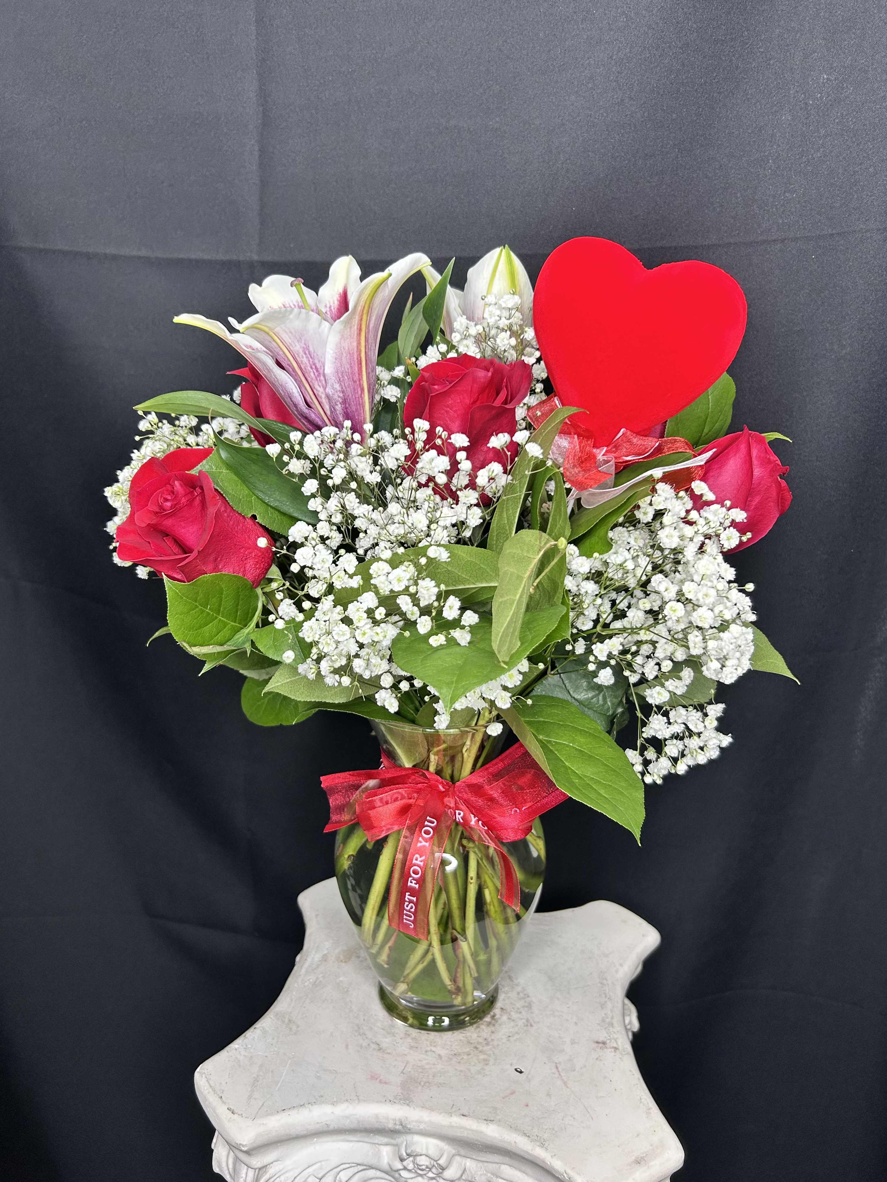 Bouquet of red roses and white lilies in a glass vase with a red heart pick