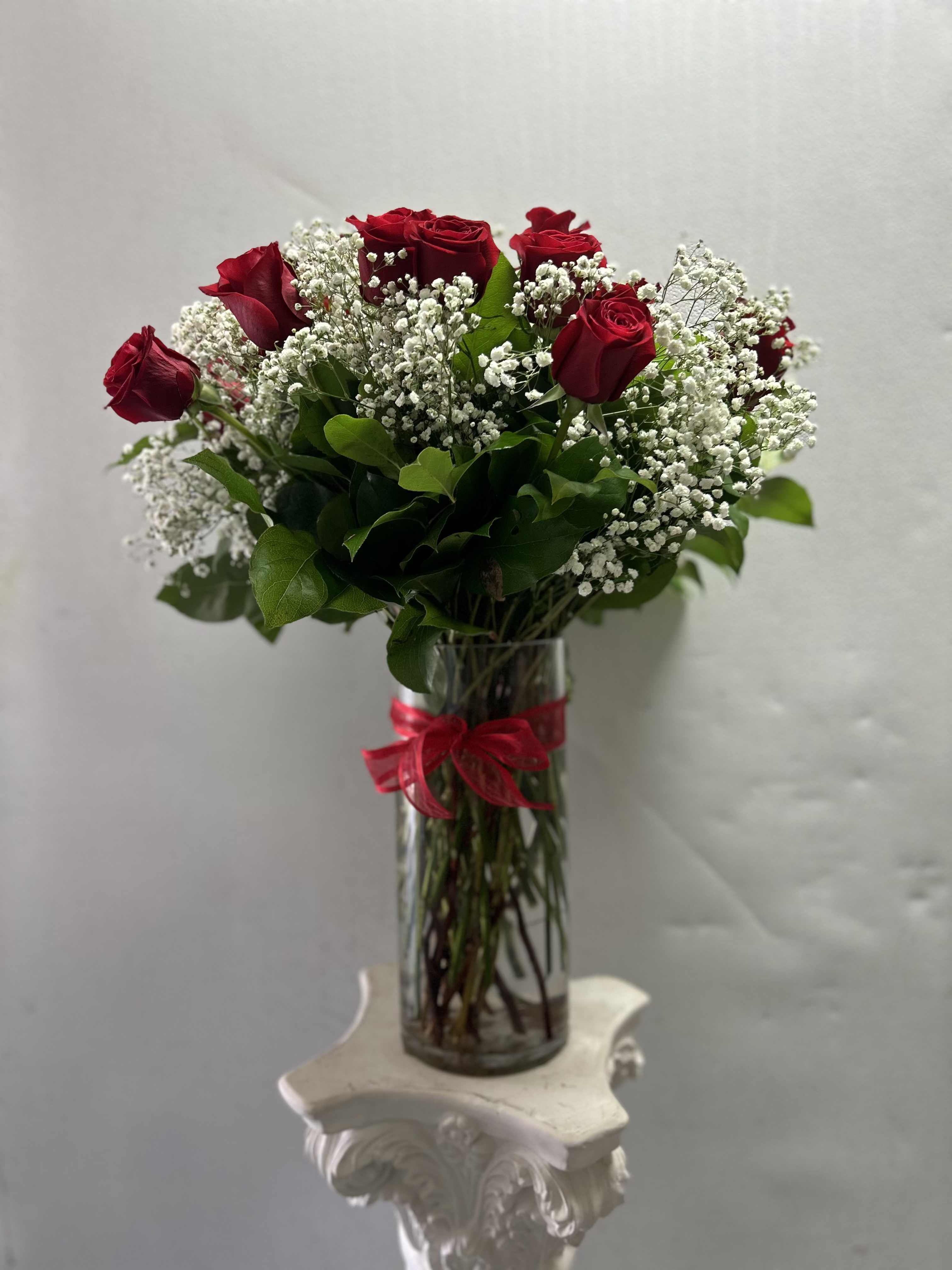 Red roses and baby's breath in a clear glass vase with a red ribbon
