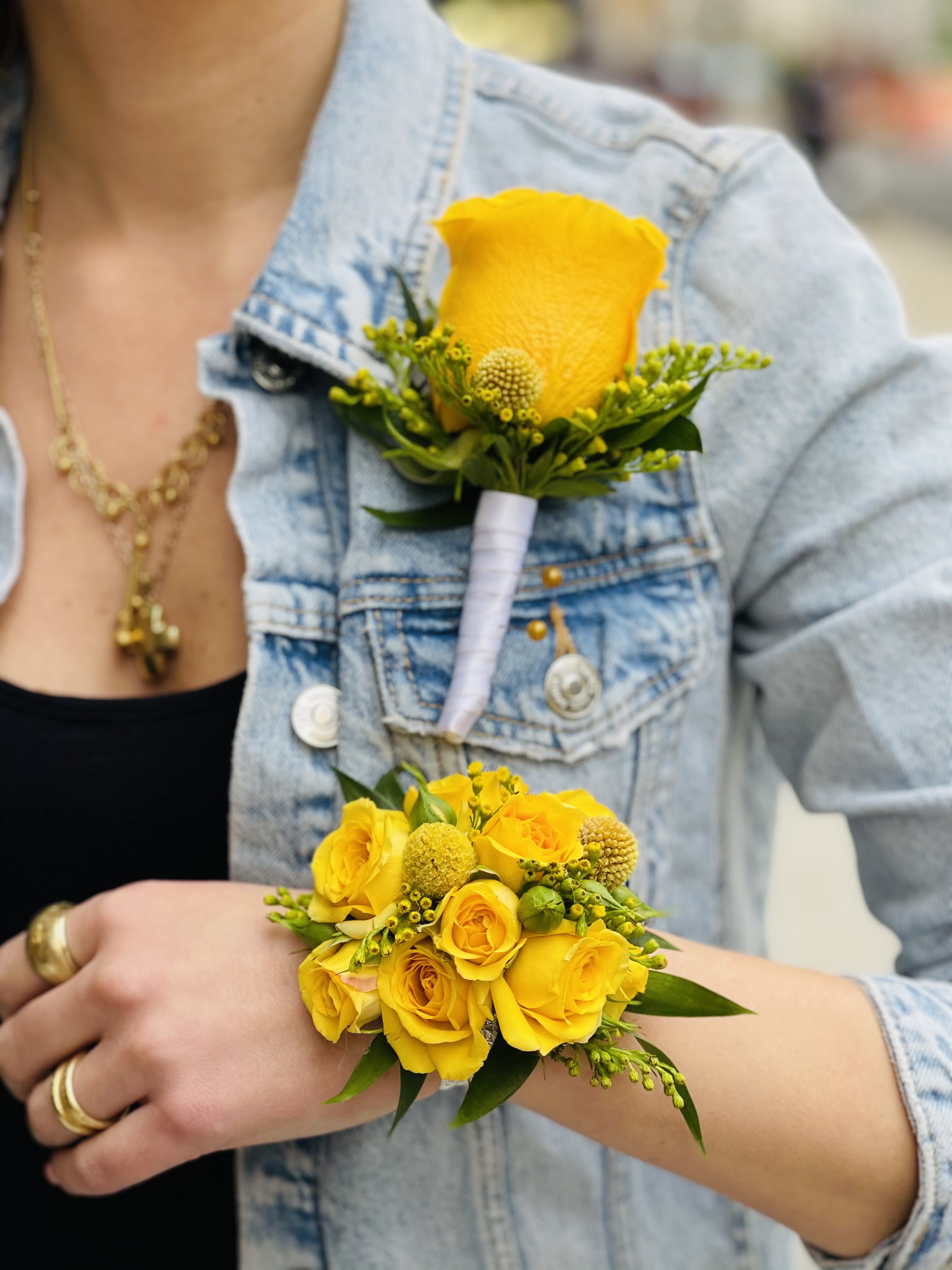 Corsage and Boutonniere Combo - A vivid yellow rose wrist corsage paired with a matching boutonniere makes an upbeat, coordinated statement for prom, weddings, or any celebratory formal event. The bright yellow palette is instantly cheerful and the compact scale keeps the look elegant and wearable-perfect for the person you want to feel seen and celebrated on their special night.  Each piece features a single yellow rose accented with small green filler and textured yellow button-like blooms for lively contrast, finished with a neat white ribbon wrap and boutonniere pin for secure wear. The wrist corsage is sized to sit comfortably without overpowering an outfit, while the boutonniere is compact and tailored for a lapel; together they create a polished, harmonious set that reads fresh, festive, and thoughtfully put together.