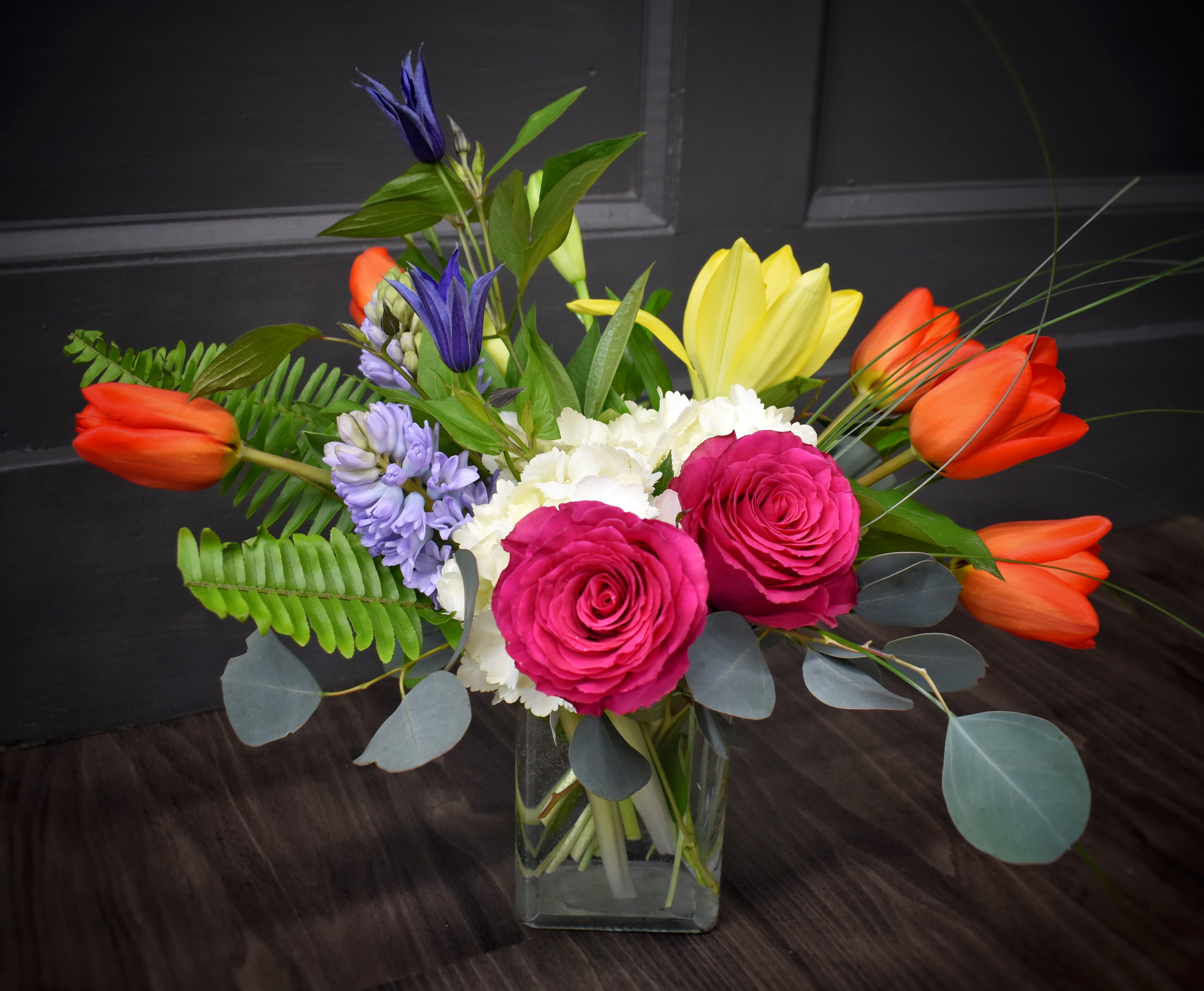 Meadow Fresh- PREMIUM - Bright pink roses and sunlit orange-and-yellow tulips mingle with white blooms and purple accents to create a joyful flower arrangement perfect for birthdays, thank-yous, or just-because celebrations. This garden-fresh flower arrangement for gifting reads bright and energetic-she'll feel noticed and celebrated the moment it arrives.  The PREMIUM bouquet is arranged in a clear glass vase with long stems and airy foliage for a full, asymmetrical silhouette that feels freshly picked. It features roses, tulips, lilies, hyacinth, and other seasonal blooms in pink, orange, white, and purple tones; the white center softens the palette while the saturated colors add cheerful contrast. The vase gives it a clean, modern finish and lets the stems show through for a natural look.  Ideal for celebrating a birthday, congratulating a friend, or sending thoughtful cheer, this arrangement is the kind of gift that brightens a room and lifts spirits. Delivered ready-to-display in the included clear glass vase; to keep flowers lasting longer, change the water every other day and trim stems slightly when refreshing the vase.