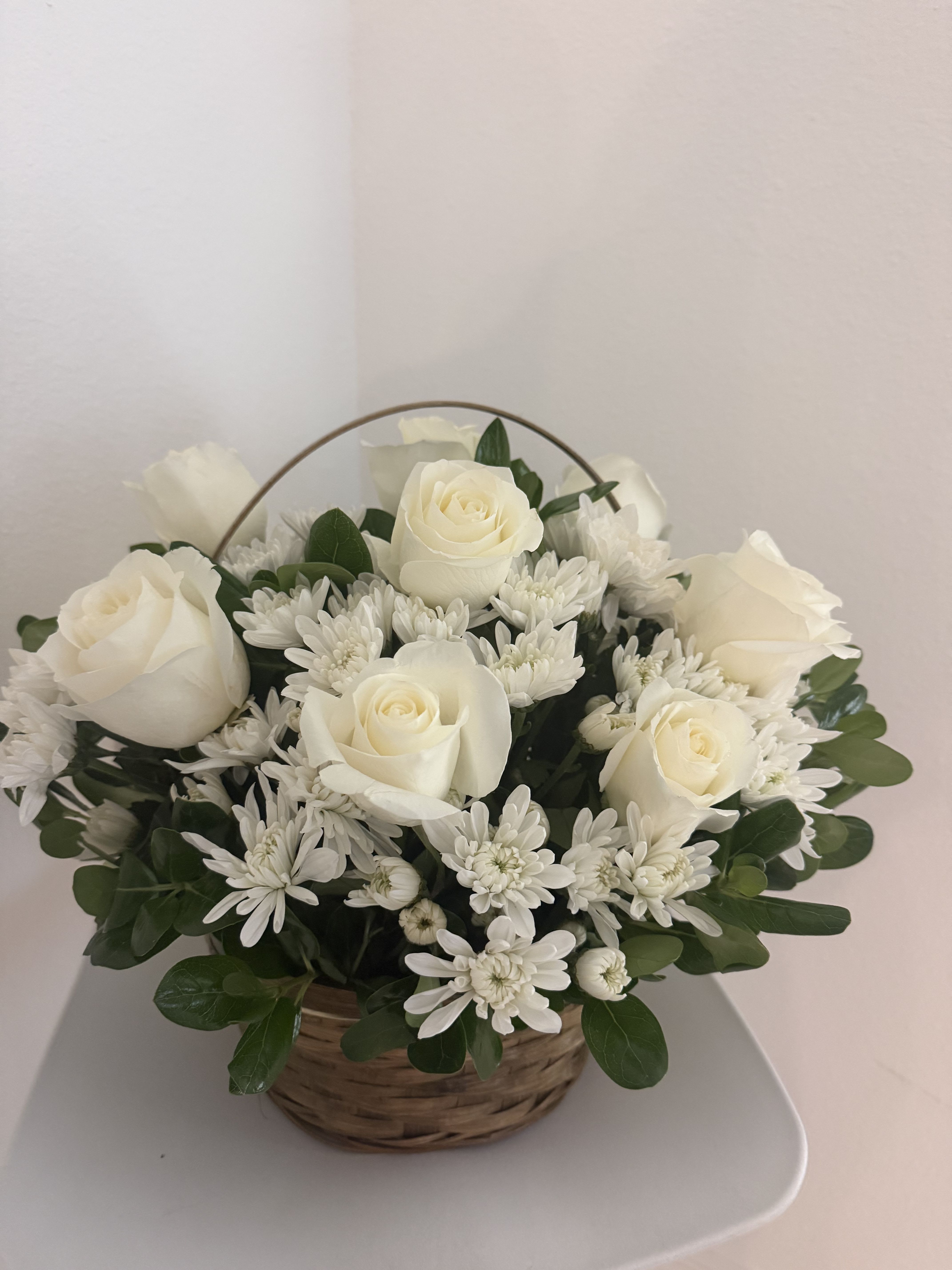 Pure Elegance Basket - A white basket arrangement with roses, daisies, and pom flowers, creating an elegant all-white design. This arrangement symbolizes purity, peace, and heartfelt sincerity, making it perfect for sympathy, special tributes, or graceful gifting.