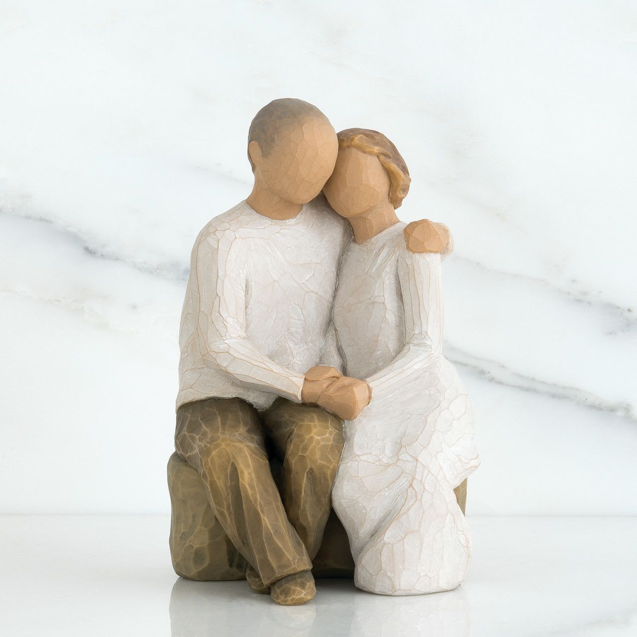 Anniversary - A carved, seated couple captured in an intimate embrace creates a quietly romantic gift for an anniversary or wedding celebration. This figurine arrangement is perfect for saying "still us" to the person you're celebrating - the warm brown tones of the figures and soft white clothing evoke comfort and enduring companionship, making it especially fitting as an anniversary keepsake or a thoughtful token for a milestone together.  The piece has a hand-carved, textured look with rustic, sentimental charm; its sculptural form reads like a small work of art that will sit beautifully on a mantel, bedside table, or office shelf. Though not a traditional bouquet, the neutral palette pairs easily with fresh flowers if you choose to add them-think creamy whites, soft greens, or pale blushes to complement the figurine without overpowering it.  Give this as a commemorative anniversary gift for the partner who treasures meaningful, lasting mementos, or as a wedding present that will remind the couple of their first years together. Compact and enduring, it requires no special care beyond dusting and arrives ready to display as a daily reminder of love.