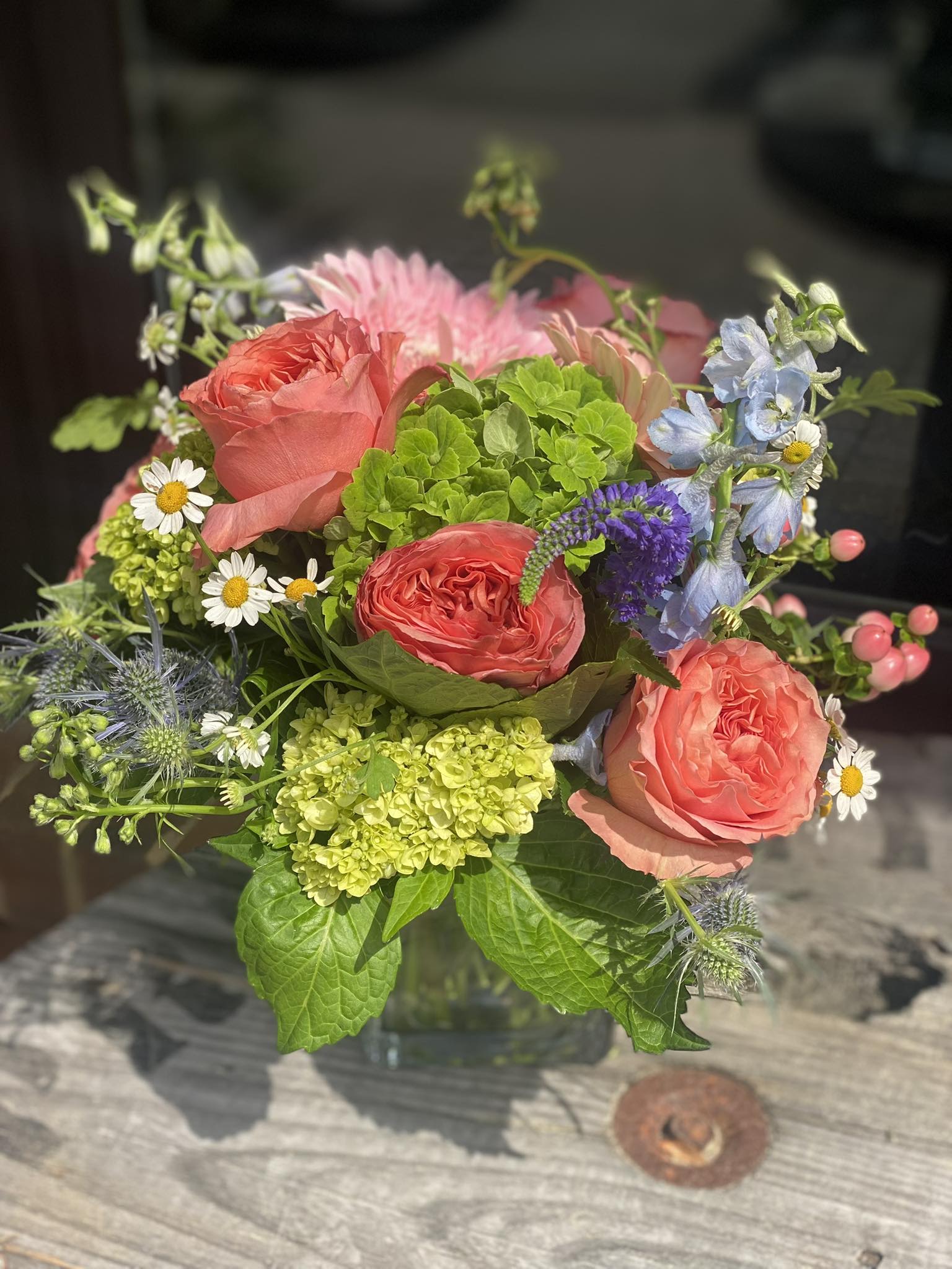 Spring Delight - A bright coral-pink rose and green hydrangea pairing gives this bouquet an instant lift-the kind of Spring arrangement that makes the person you're thinking of smile the moment it arrives. The composition reads fresh and cheerful with lively contrasts between warm orange-peach tones and cool blues.  Give this to someone who deserves to feel noticed-she'll feel genuinely celebrated by the color and light it brings into a room. Ships ready to display in the included glass vase; trim stems and refresh water every few days to keep blooms lively.