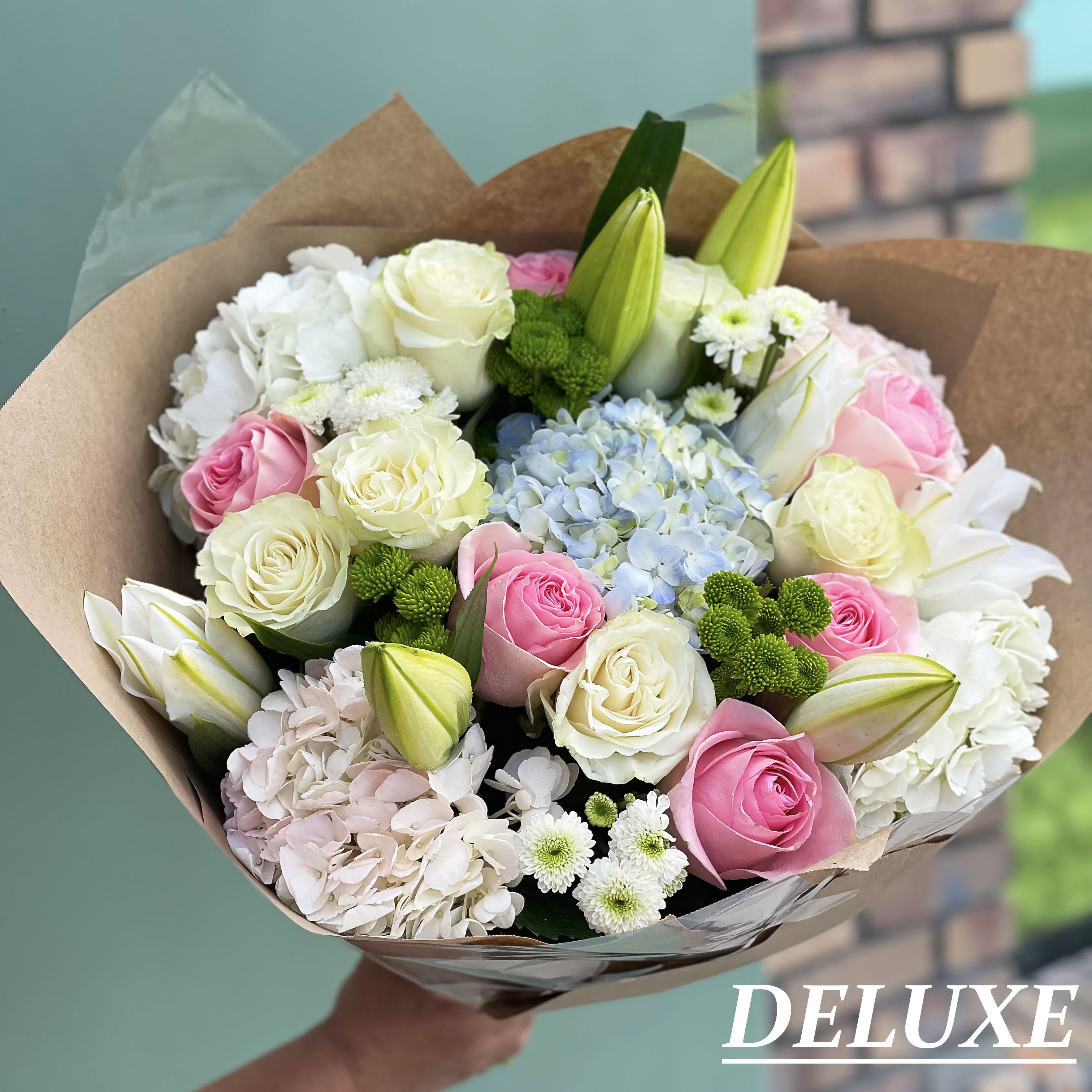 Soft Serenade - A beautifully curated deluxe bouquet featuring soft pink and white roses, delicate hydrangeas, and fresh seasonal blooms, artfully arranged for an elegant presentation. Perfect for celebrations, heartfelt gifts, or simply brightening someone’s day. This arrangement delivers a fresh, graceful charm that suits any occasion.  NOTE: The picture shown is the DELUXE VERSION 