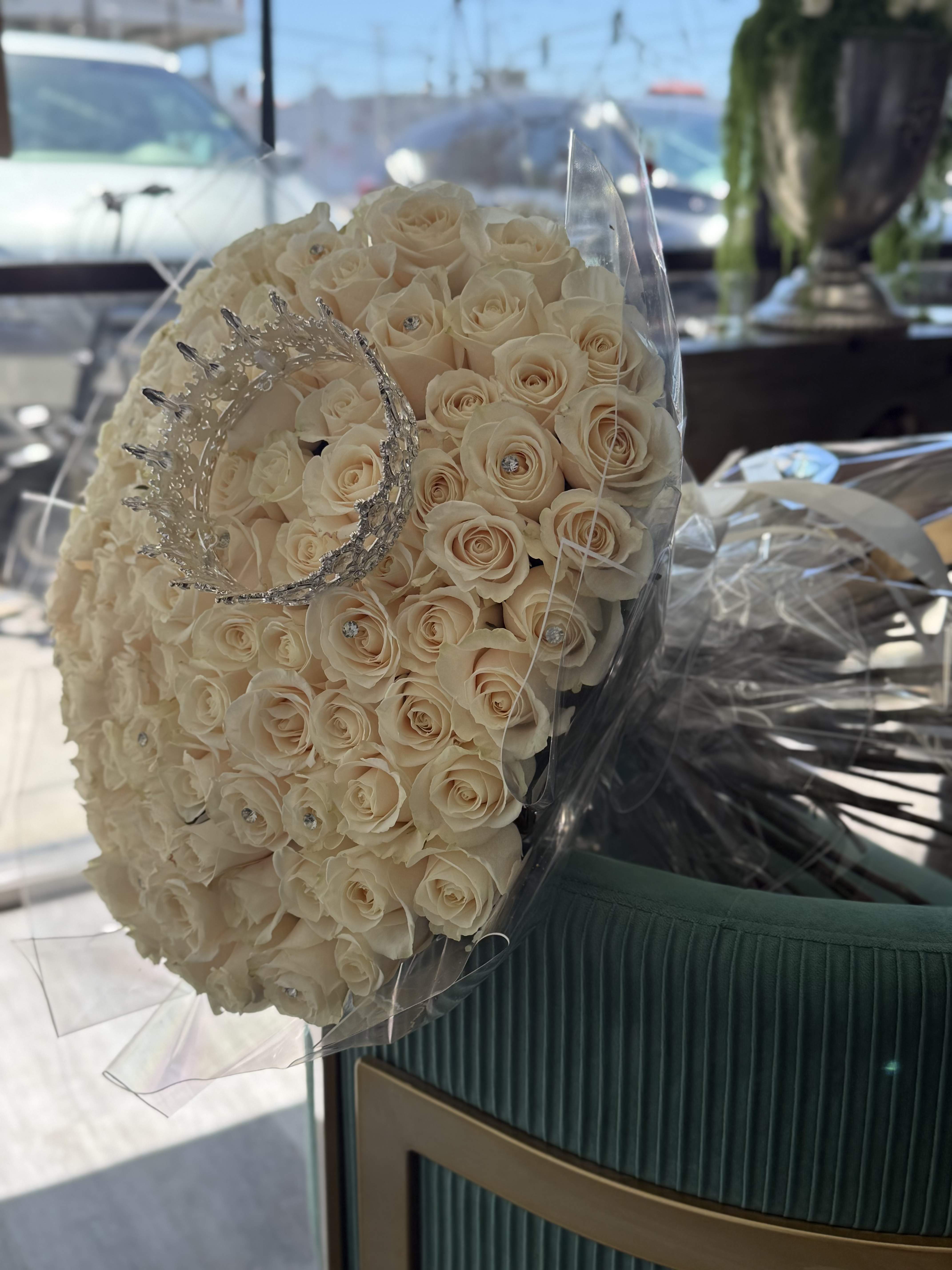 Crown Rose Bouquet - A statement of elegance and luxury, the Royal Ivory Crown Rose Bouquet features premium ivory roses hand-arranged in a grand dome style and finished with sparkling crystal accents. Topped with a regal silver crown, this bouquet is designed for queens, birthdays, bridal celebrations, quinceañeras, anniversaries, and unforgettable moments. Wrapped in luxe presentation film for a sophisticated finish, it’s more than flowers—it’s a royal experience.