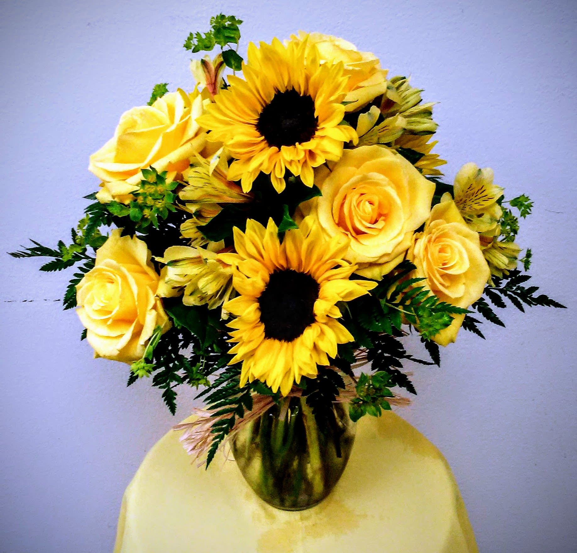 Yellow roses and sunflowers arranged in a glass vase