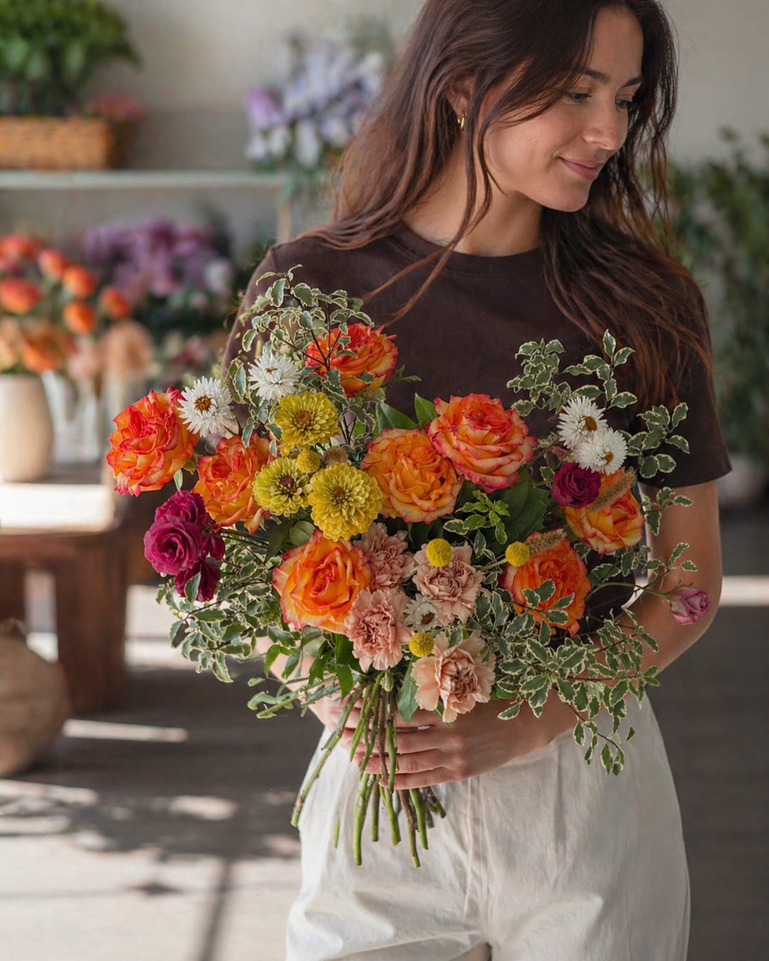 Sunset Garden Rose Bouquet - A lively mix of orange and pink roses gives this hand-tied flower arrangement a sunset glow-perfect as a birthday bouquet, anniversary gift, or just-because surprise for someone who delights in warm, cheerful color. The Sunset Garden Rose Bouquet reads romantic and fresh at once, sending a message of affection and bright celebration that will make the person you're thinking of feel truly seen.  This loose, garden-style bouquet pairs saturated roses with pale peach carnations, white daisy-like blooms, and sunny yellow chrysanthemums, all framed by variegated greenery for a textured, airy finish. The informal, freshly gathered shape creates natural movement and a soft, tactile look; the combination of textures-velvety rose petals, ruffled carnations, and crisp daisy centers-invites close-up appreciation.  Ideal for everyday celebrations and milestone moments alike, this arrangement suits recipients who love a relaxed, romantic aesthetic. Hand-tied for a casual, abundant feel, it arrives ready to display in a vase; refresh the stems in clean water every few days and trim ends to extend vase life.