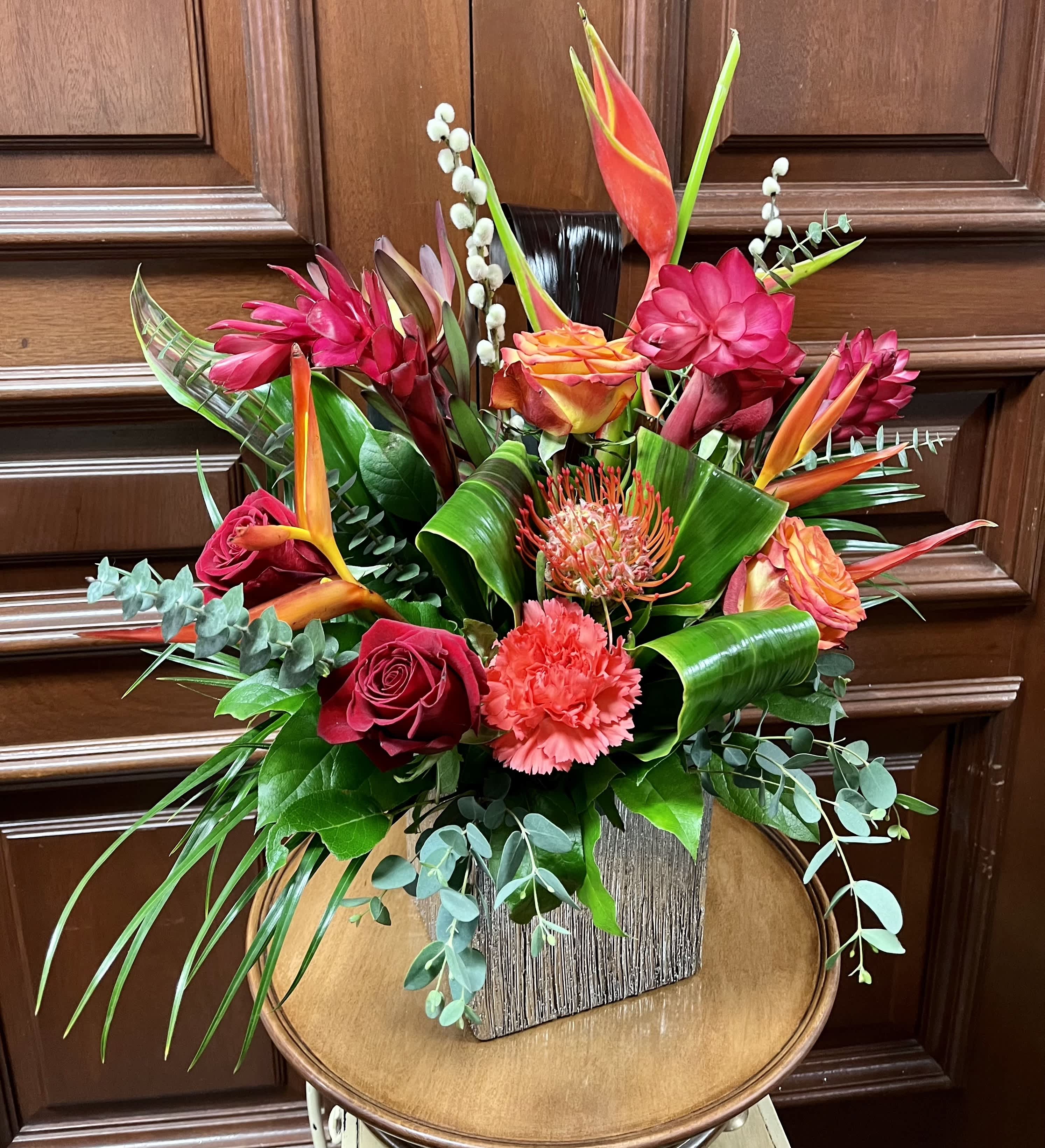 Tropical bouquet with red roses, orange bird of paradise, and pink blooms in a wooden vase