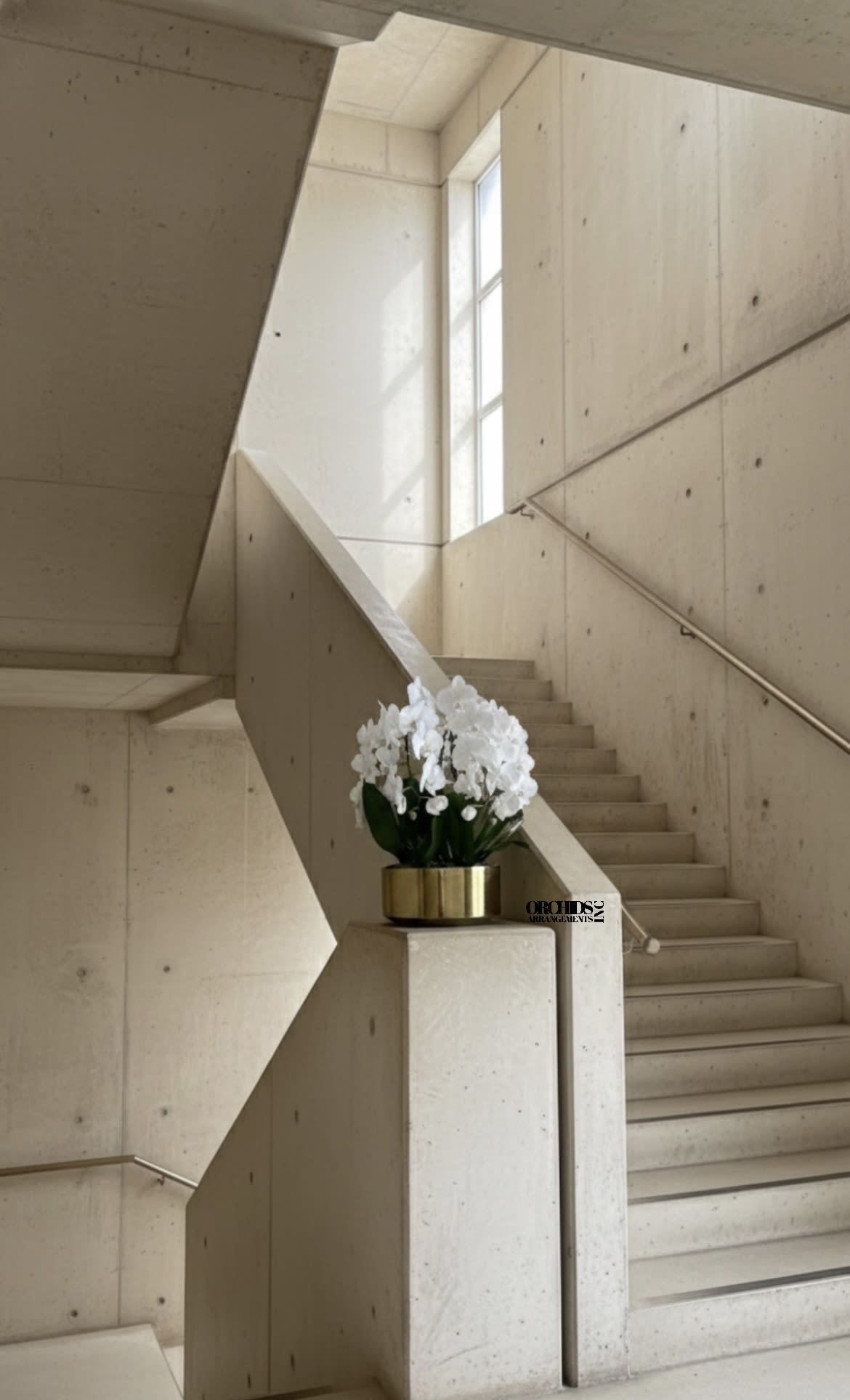 White orchids arranged in a gold planter on a stair landing