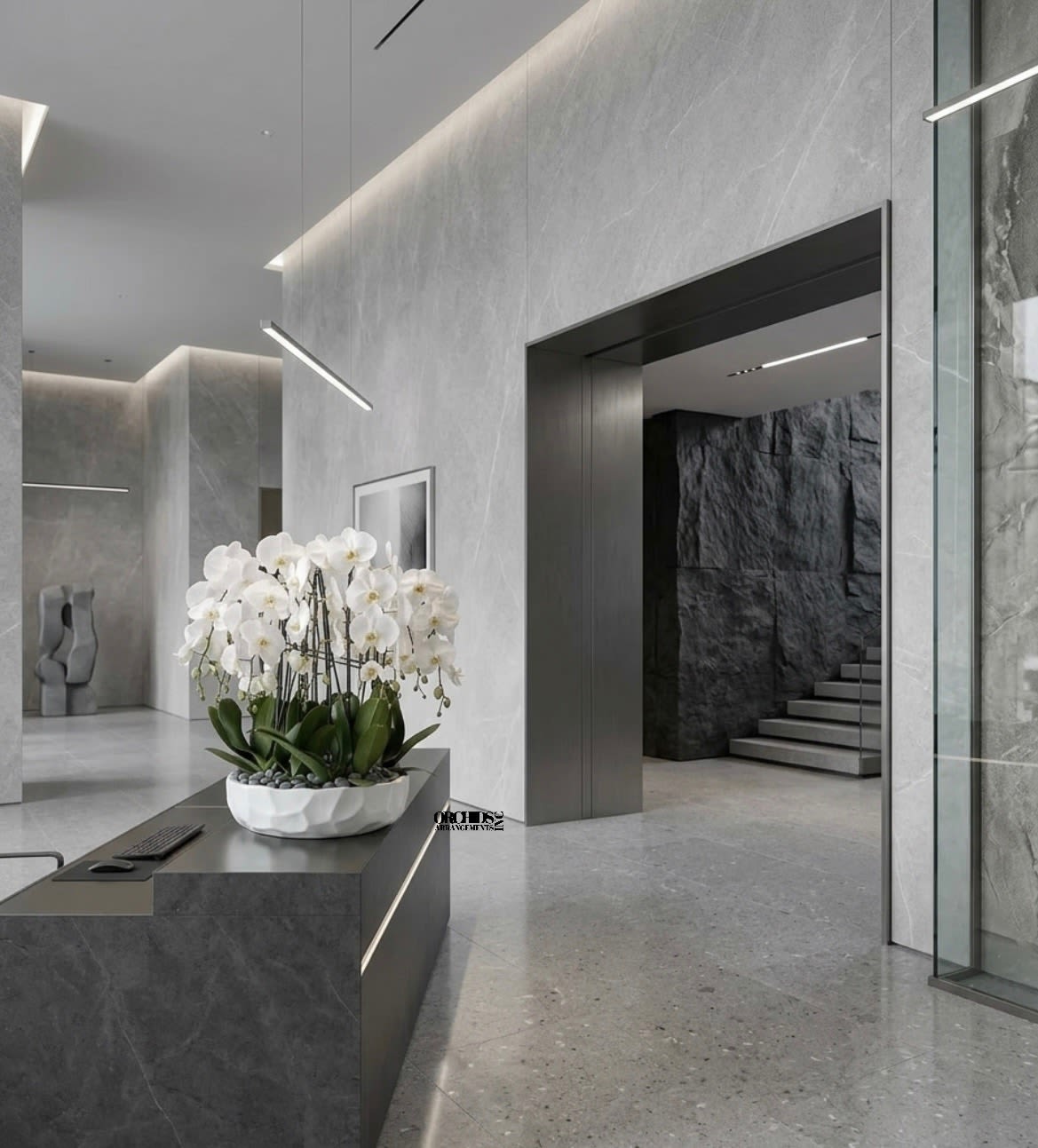 White phalaenopsis orchids in a low white bowl planter with stones on a modern gray reception desk