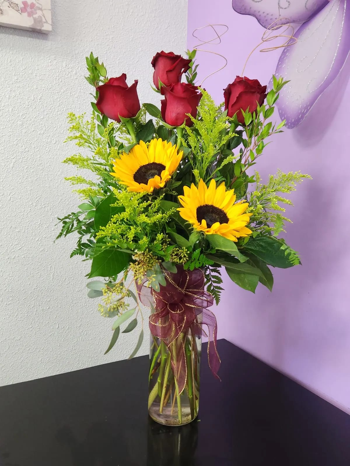 Red roses and sunflowers in a clear glass vase with ribbon