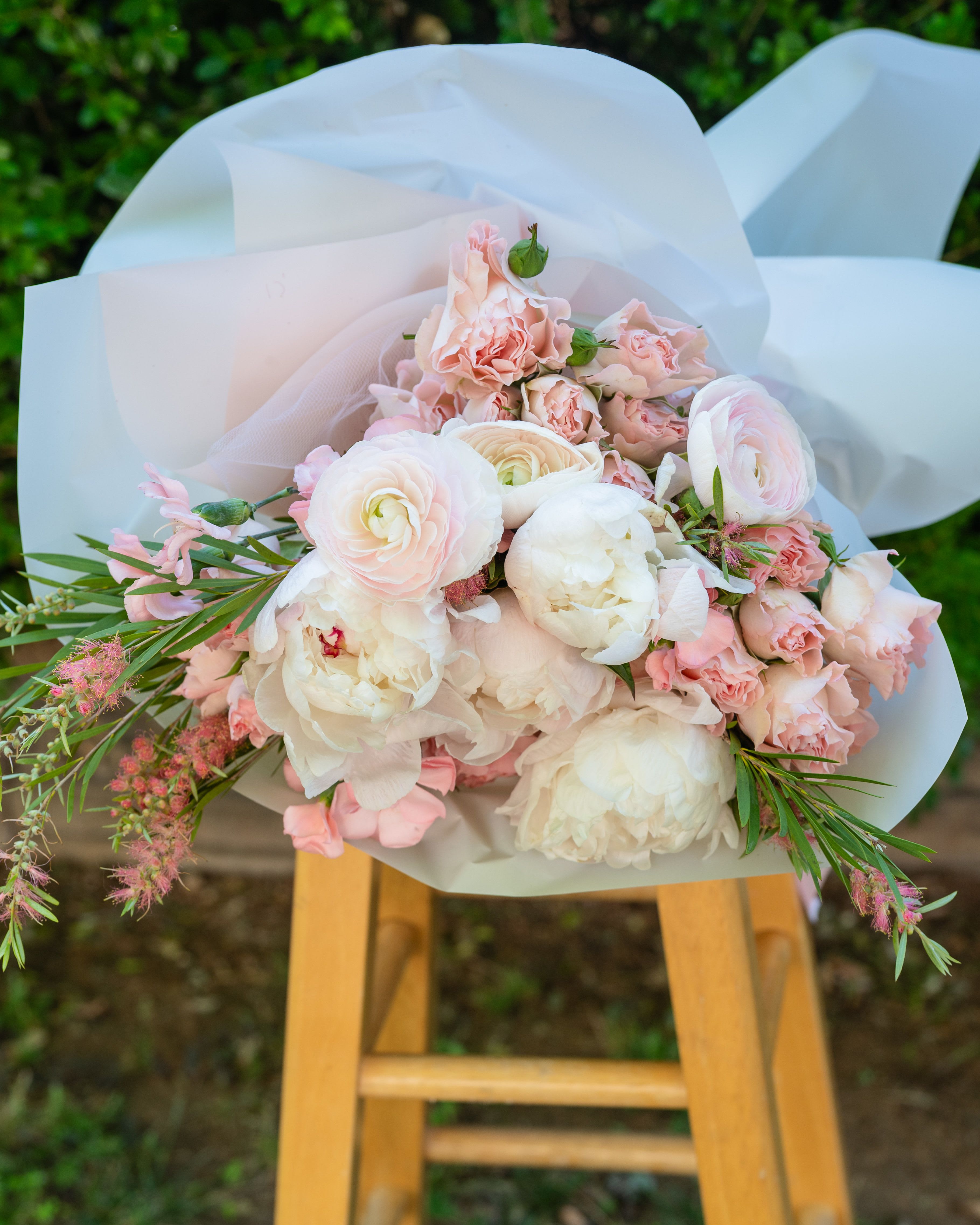 Petal &amp; Grace - There is a kind of beauty that doesn't announce itself. It simply arrives… full, soft, and completely unforgettable. Petal &amp; Grace is a celebration of that beauty. A lush gathering of white peonies, blush ranunculus, and spray roses, each bloom chosen for its softness and layered together with the kind of care that can only be felt. Wrapped in soft white paper and presented inside our signature matte black Romance by Shakira bag, this bouquet arrives as a complete experience… the drama of the black, the tenderness of the blooms, the quiet luxury of every detail. It is the bouquet that feels like a gift before it is even unwrapped. For the mother who carries everything with grace. For the woman who deserves to be celebrated in full bloom. For anyone who has ever loved someone and wanted them to feel it completely. Petal &amp; Grace. Because she always has been.