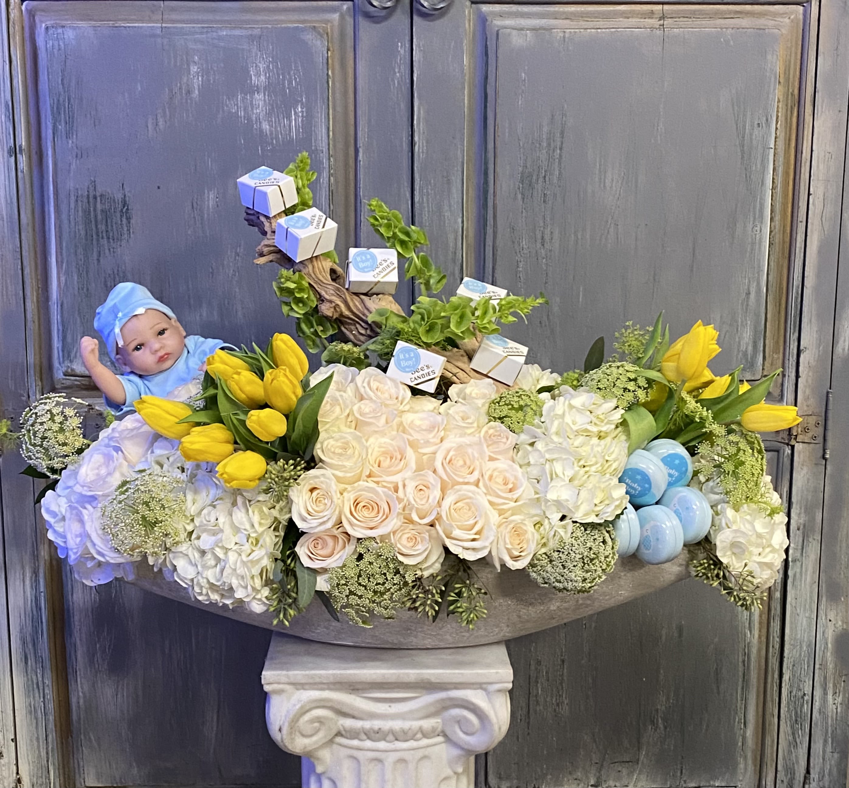 Floral arrangement with yellow tulips, pale roses, and a baby doll.