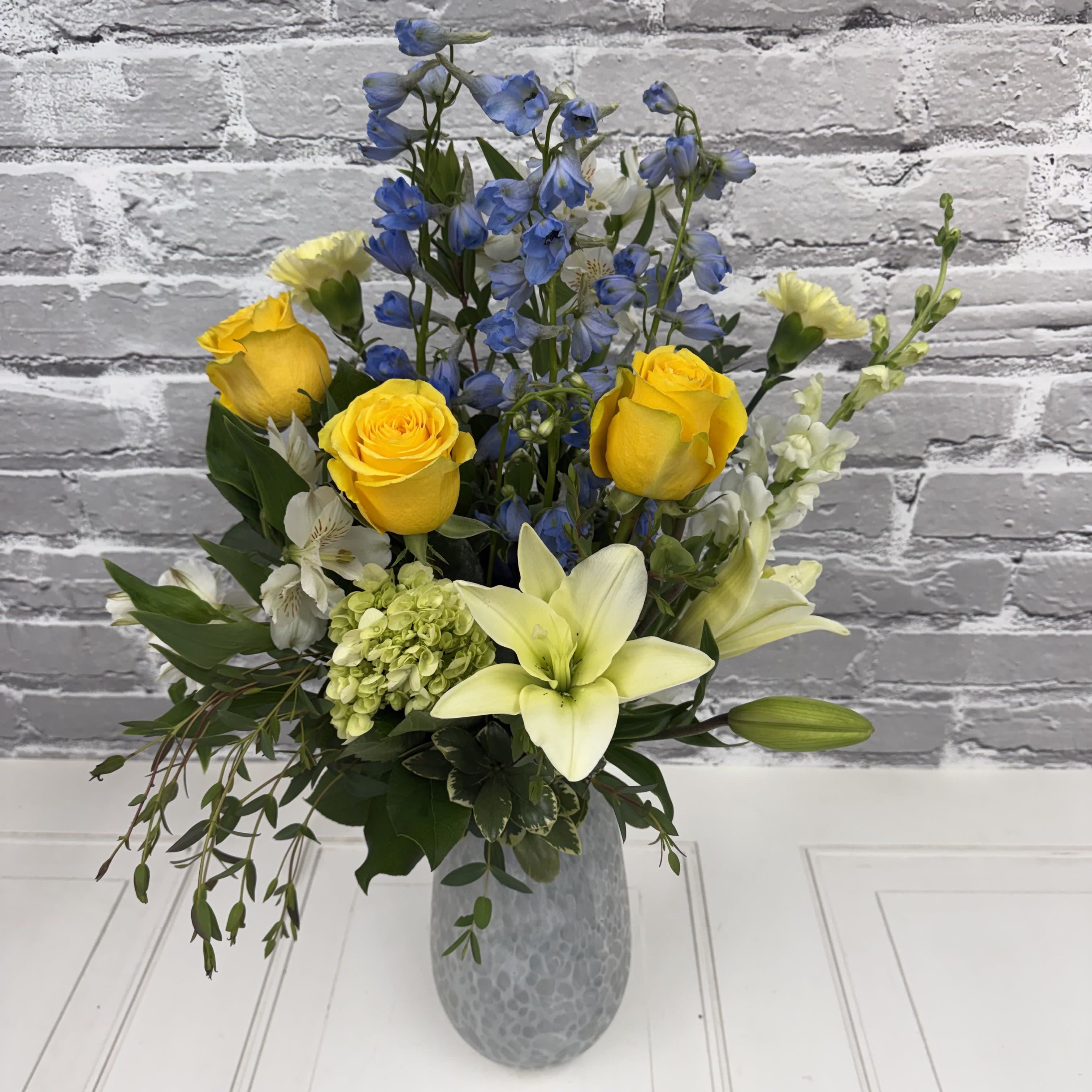 Dear Mom, - Gorgeous hand-blown vase with a white iridescent finish! Beautiful yellow, white and blue blooms are added to create a beautiful flower arrangement.