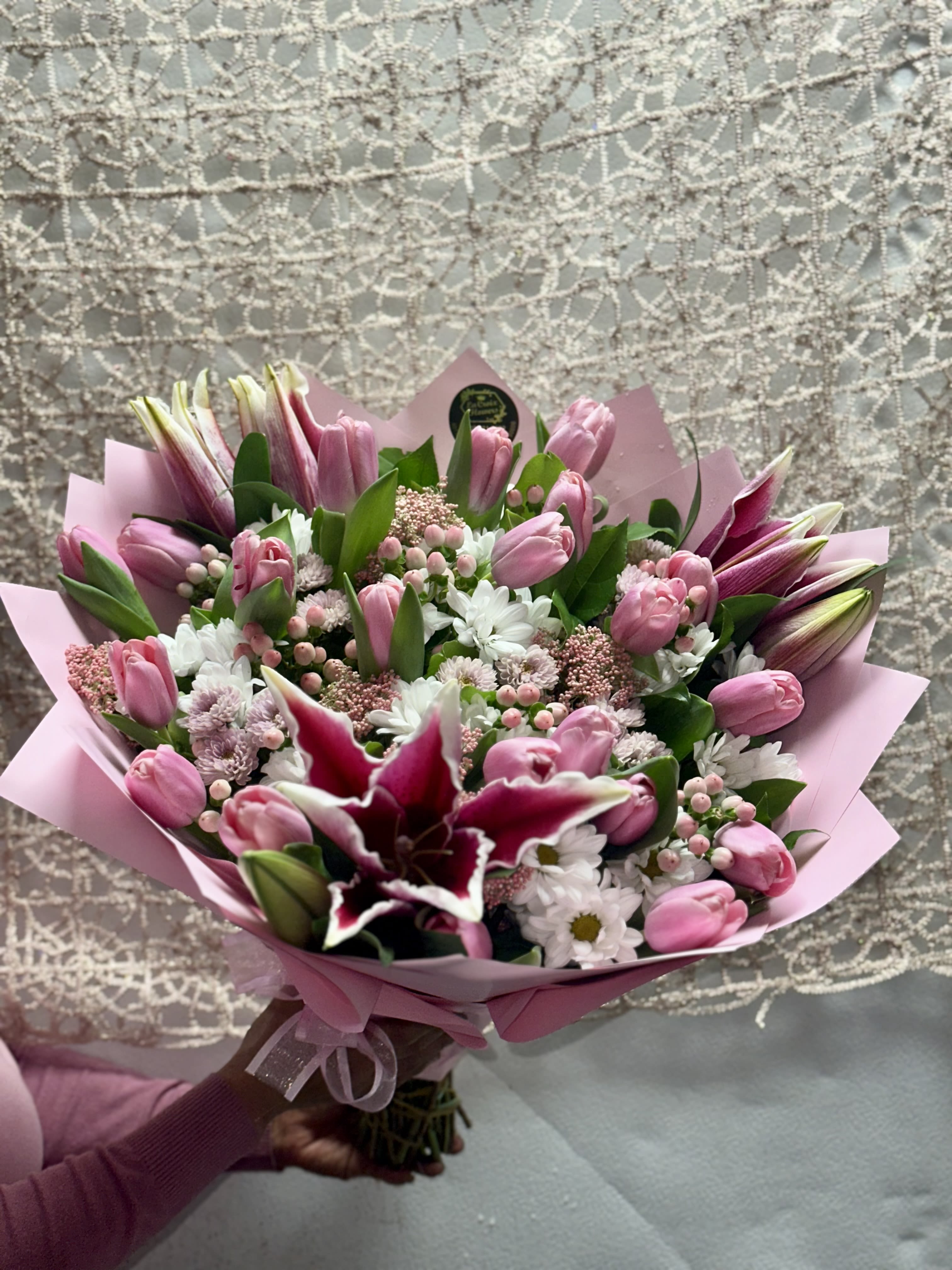 Pink tulip bouquet with white daisies and a dark lily in pink wrap