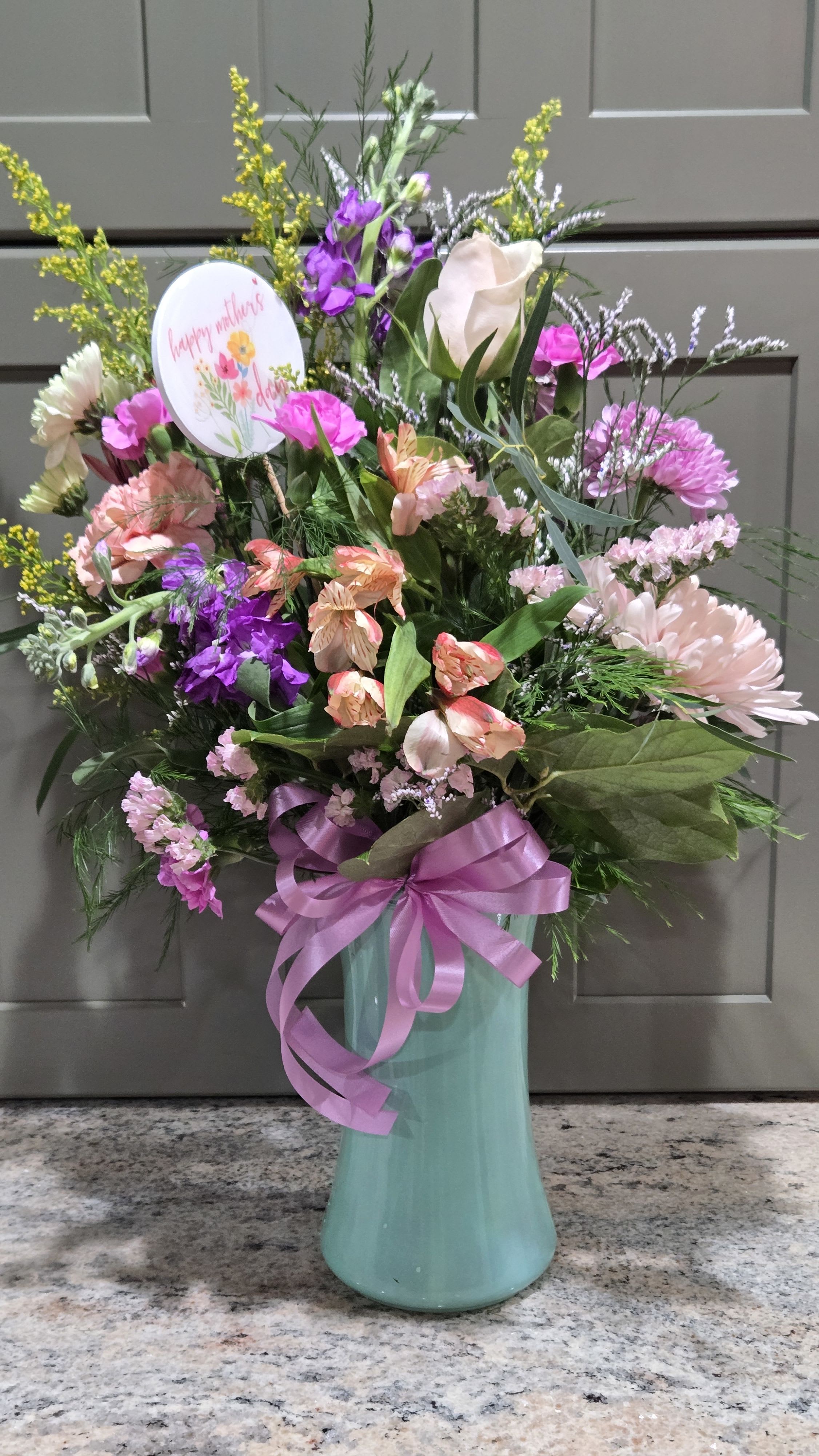 Mom Rocks - Mom's will appreciate this cheerful design variety. Circular style, with a Happy Mother's Day holiday pick,I Lavender bow finishes the holiday design. Soft pastel variety in a glass gathering vase. Minty green tone (while supplies last) other colors or clear are available as we get closer to Mother's Day!