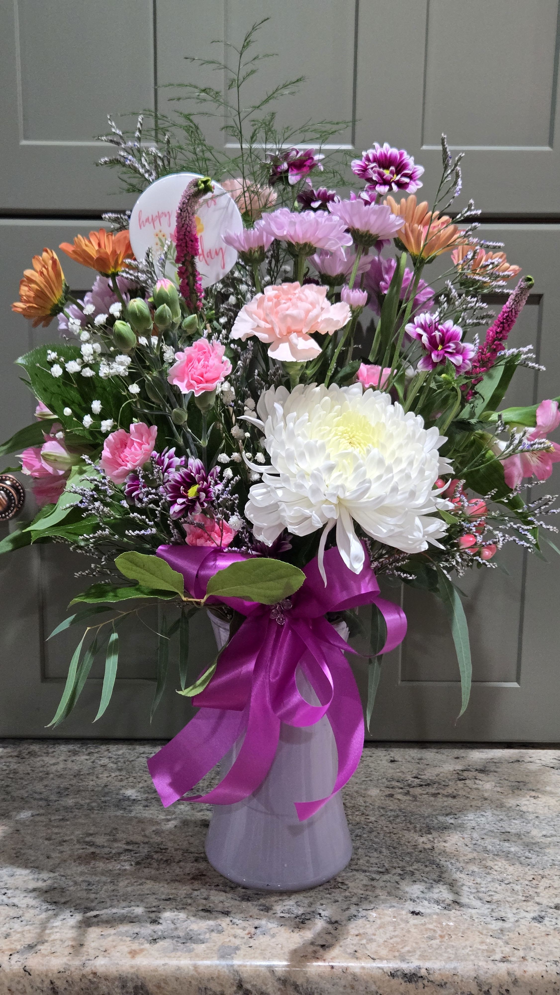 Mom's a Star - Glass gathering vase of market fresh flowers, fillers, and mixed greens. Softer pastel tones, Lavender bow and vase while supplies last. Happy Mother's Day pick!