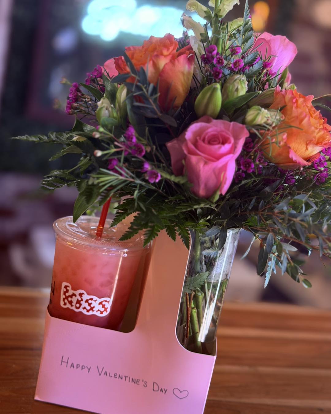 Pink and orange roses in a clear vase beside a pink drink cup.