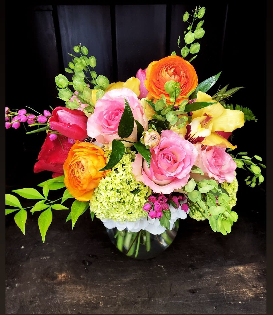 Colorful bouquet of roses, ranunculus, and orchids in a glass vase
