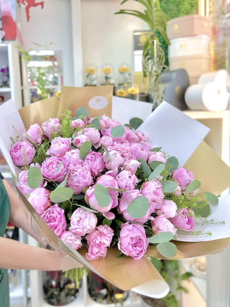 Large hand-tied bouquet of pink peonies wrapped in white and gold paper