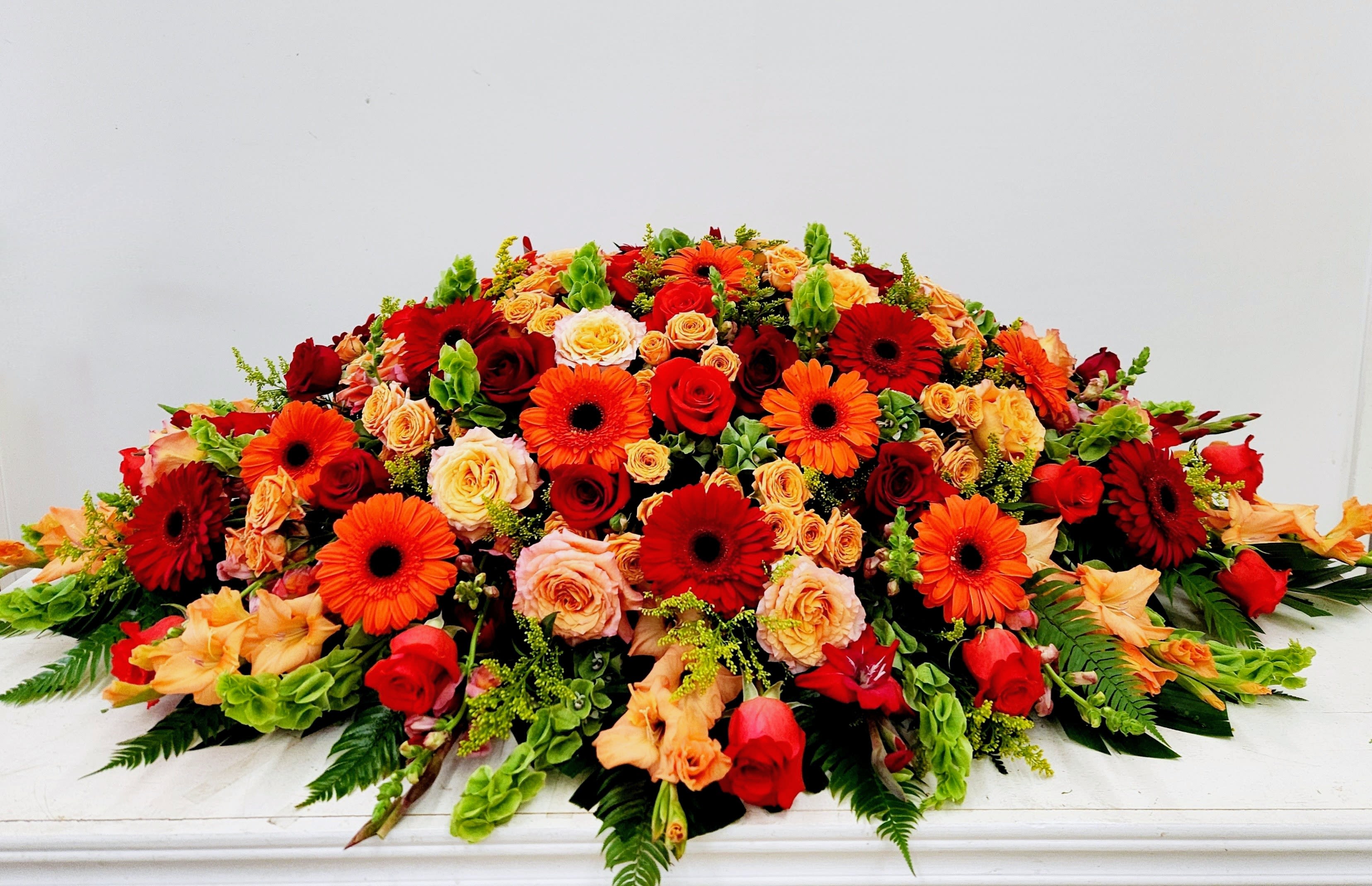 Colorful Life Casket Spray - A bold, full-bodied tribute that reads more like a celebration of life than a somber spray, this colorful life casket spray pairs gerbera daisies and roses in a warm palette of red, orange, peach, yellow and green to create a vibrant, comforting statement for sympathy and funeral services. The wide, low, sprawling shape lays beautifully across a casket or service table and gives the person you're honoring a radiant focal point that feels both respectful and joyfully alive.  Choose this spray when you want the recipient's family to feel comforted and seen-an arrangement that honors traditions while reflecting the vibrant life remembered. As a large, low centerpiece-style design, it arrives ready to place and maintain its lush, packed look through services; please contact us with specific size or placement requests so we can tailor the final composition to the setting. CALL A BEAUTIFUL CALIFORNIA at 562-437-4106 or visit us at 611 E Carson Street, Suite B, Long Beach CA 90807.