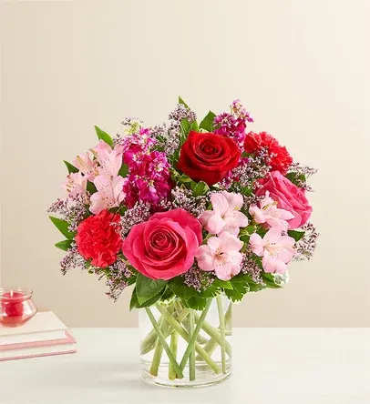 Bouquet of red and pink roses with pale pink flowers in a clear glass vase