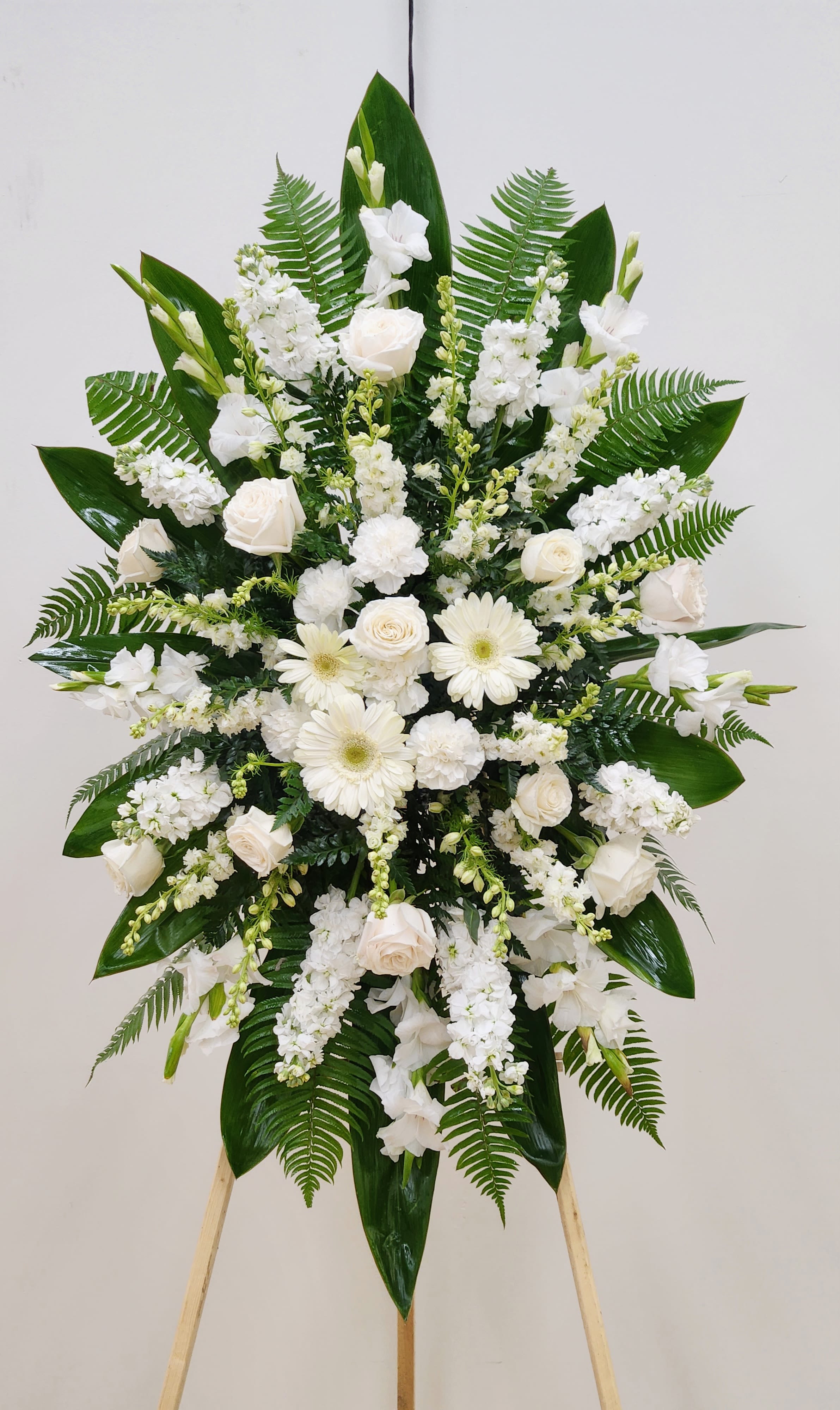 Tranquility - A serene white standing spray crafted to convey deep sympathy and quiet reverence, Tranquility is a large funeral or memorial arrangement that honors the life of the person you're remembering. The easel-mounted presentation and formal, symmetrical design make this flower arrangement a respectful choice for a graveside service or memorial gathering, offering a calm visual focus that helps family and friends pause and reflect.  