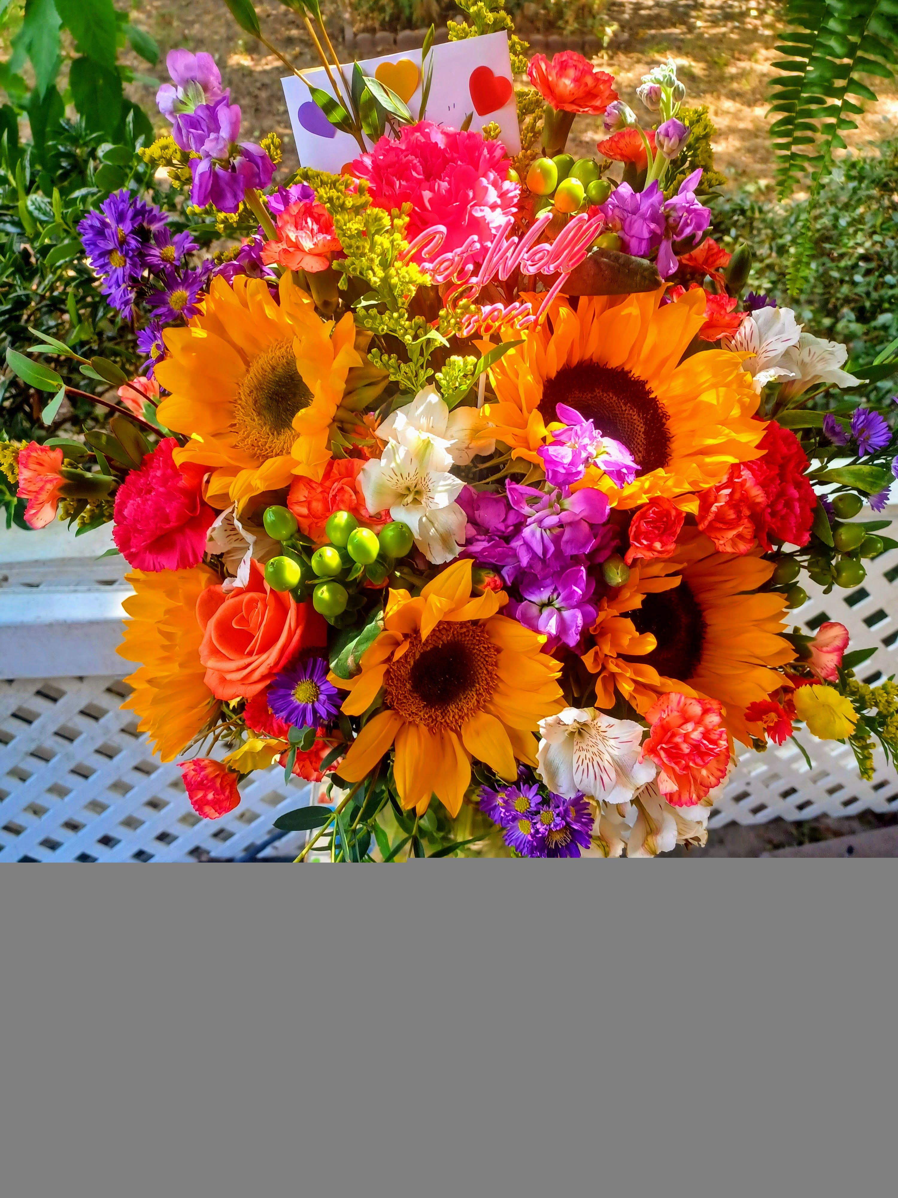 Sunny Sunflowers - A bright pretty mixture of sunflowers, purple stock, orange roses and other vibrant colored filler flowers designed in a vase or basket(specify your choice in special instructions)