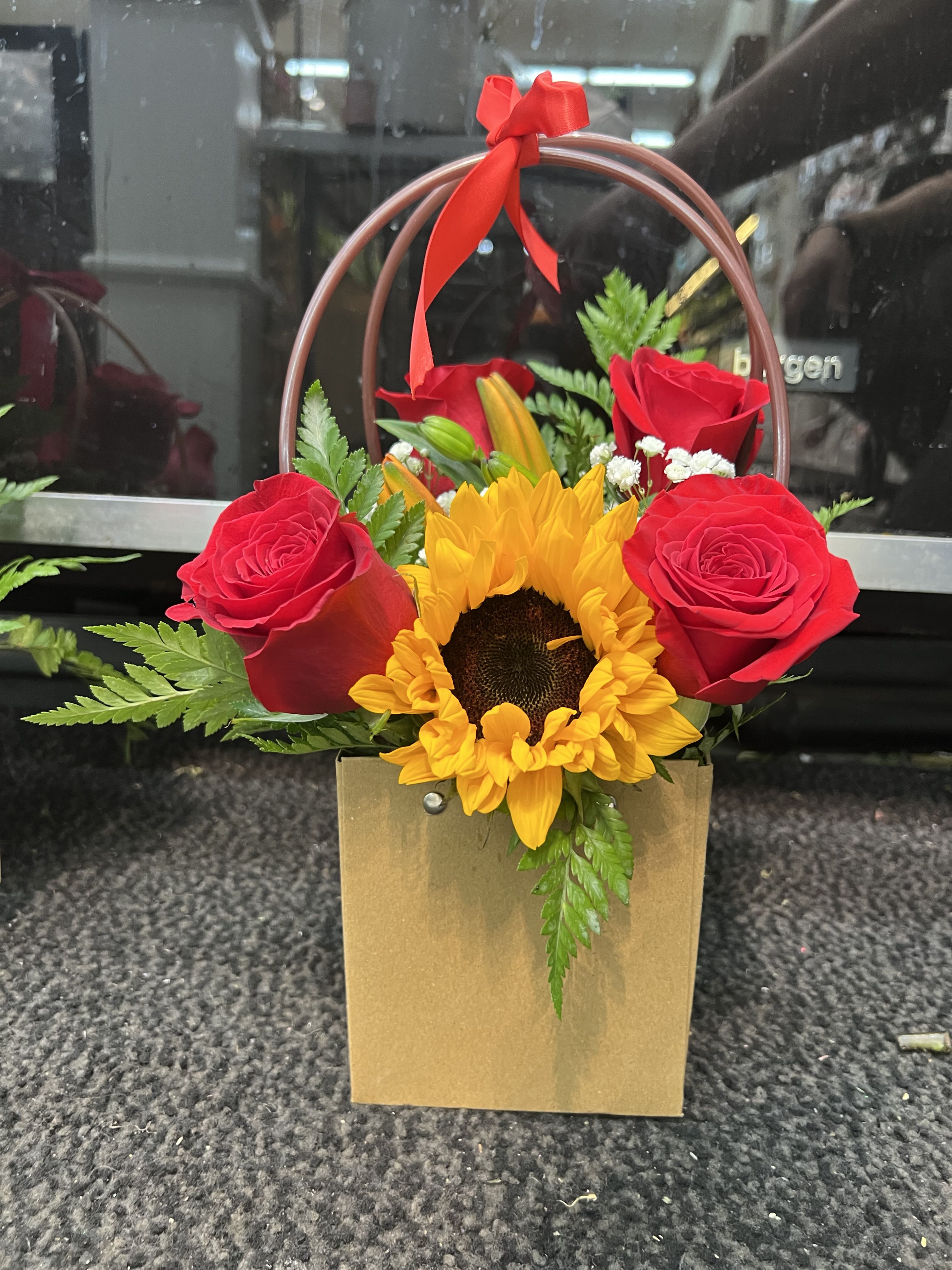 Red roses and a sunflower in a gold gift bag with a red ribbon