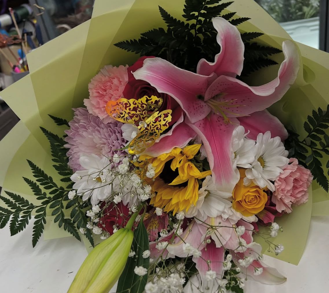Bouquet of pink lilies, roses, daisies, and carnations wrapped in pale green paper