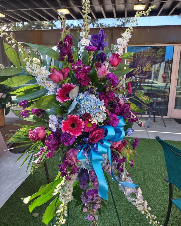 Tall floral standing spray with purple, pink, and blue flowers and a blue ribbon