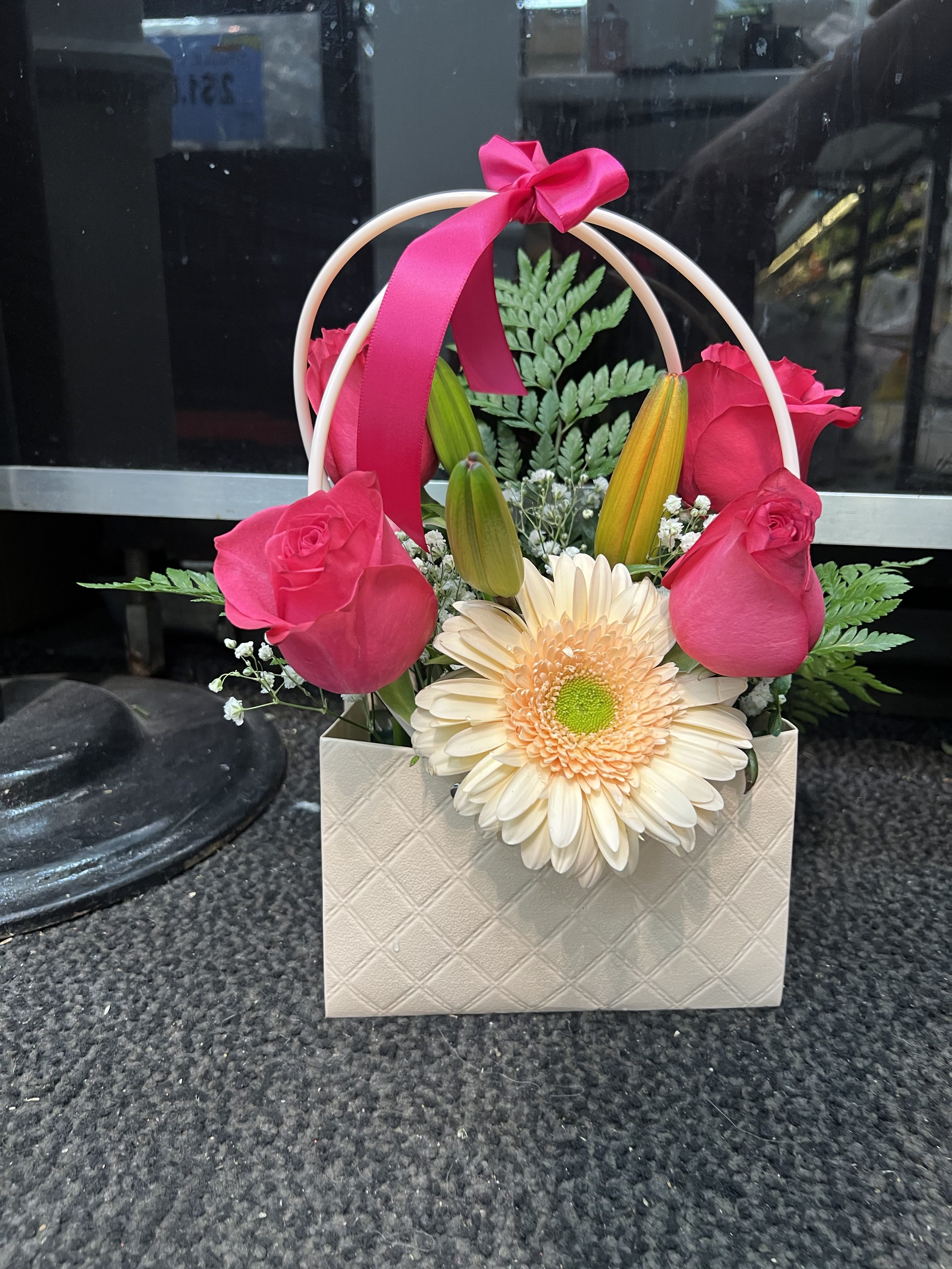 Pink roses and a cream gerbera daisy in a gift bag with a ribbon handle